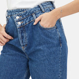 Eine Person trägt eine hochgezogene Blue Jeans, ein weißes Oberteil und präsentiert das Tamaris Armband - The Love Heart by Tamaris mit einer Hand in der Tasche.