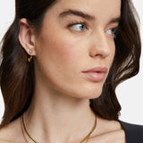 Frau mit gewelltem braunem Haar, in einem schwarzen Oberteil und zwei goldenen Halsketten, schaut zur Seite und trägt den Tamaris Ohrring - The 2 in 1 Creole von Tamaris.