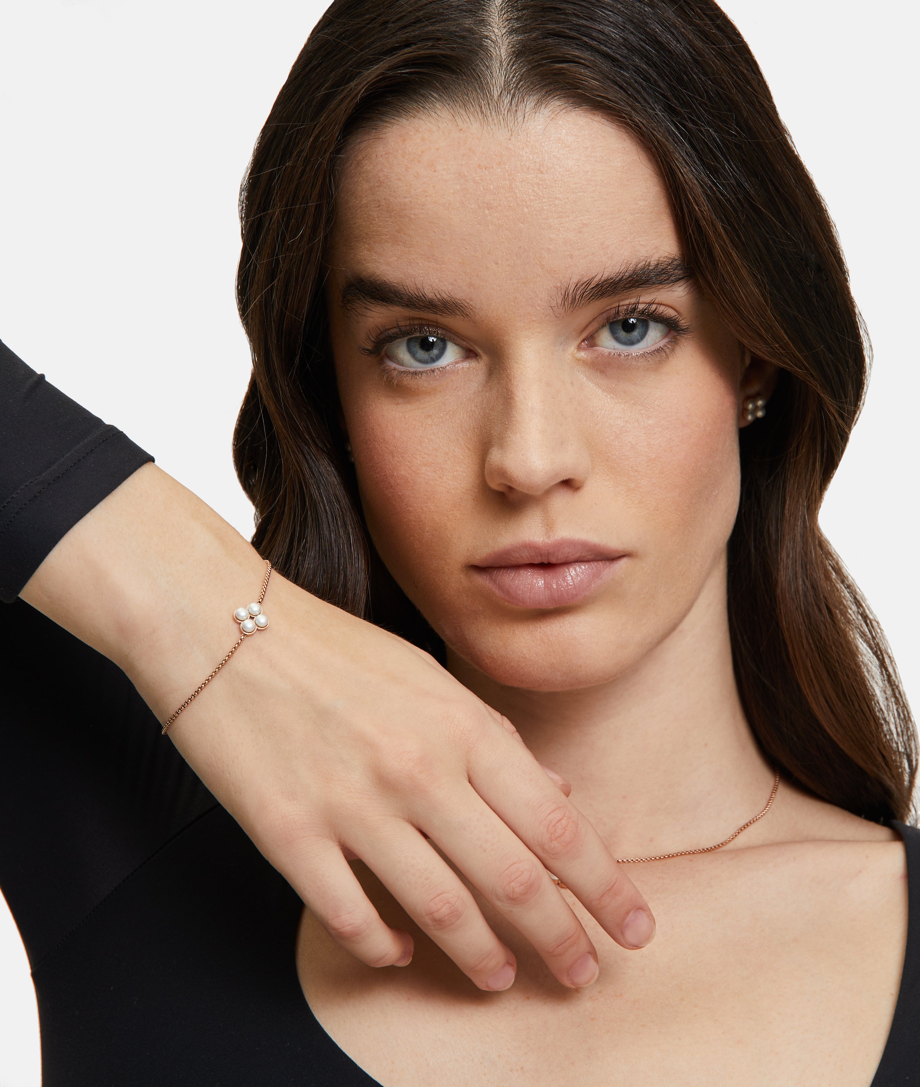 Eine Frau mit langen braunen Haaren trägt das Tamaris Armband - The Flower Pearl von Tamaris, gepaart mit Perlenohrringen und einer floralen Halskette mit Glasperlenanhänger, und posiert anmutig.