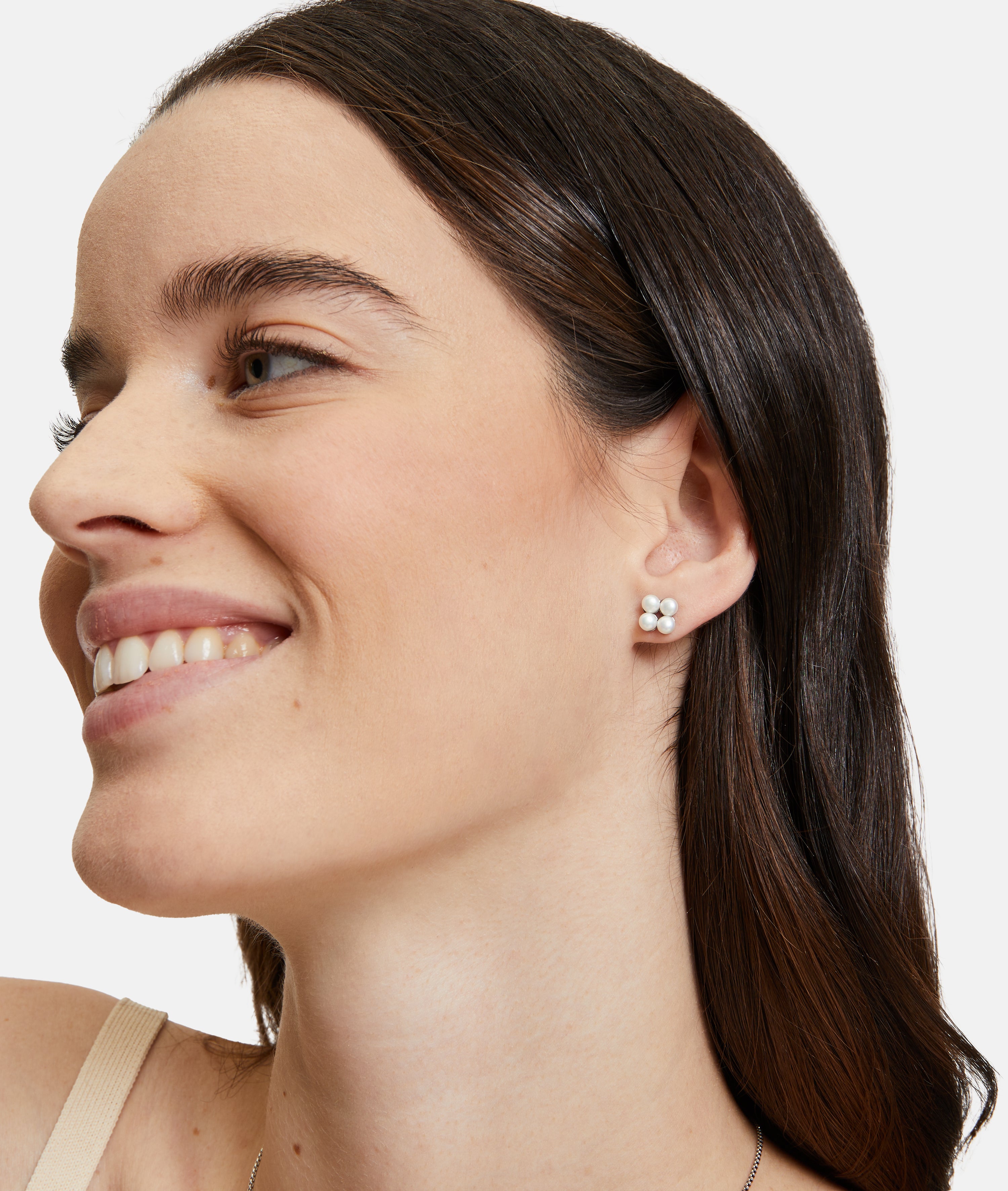 Eine Frau mit glattem braunem Haar und natürlichem Make-up lächelt, während sie Tamaris Ohrstecker - The Flower Pearl, einen floralen Ohrring von Tamaris, trägt.