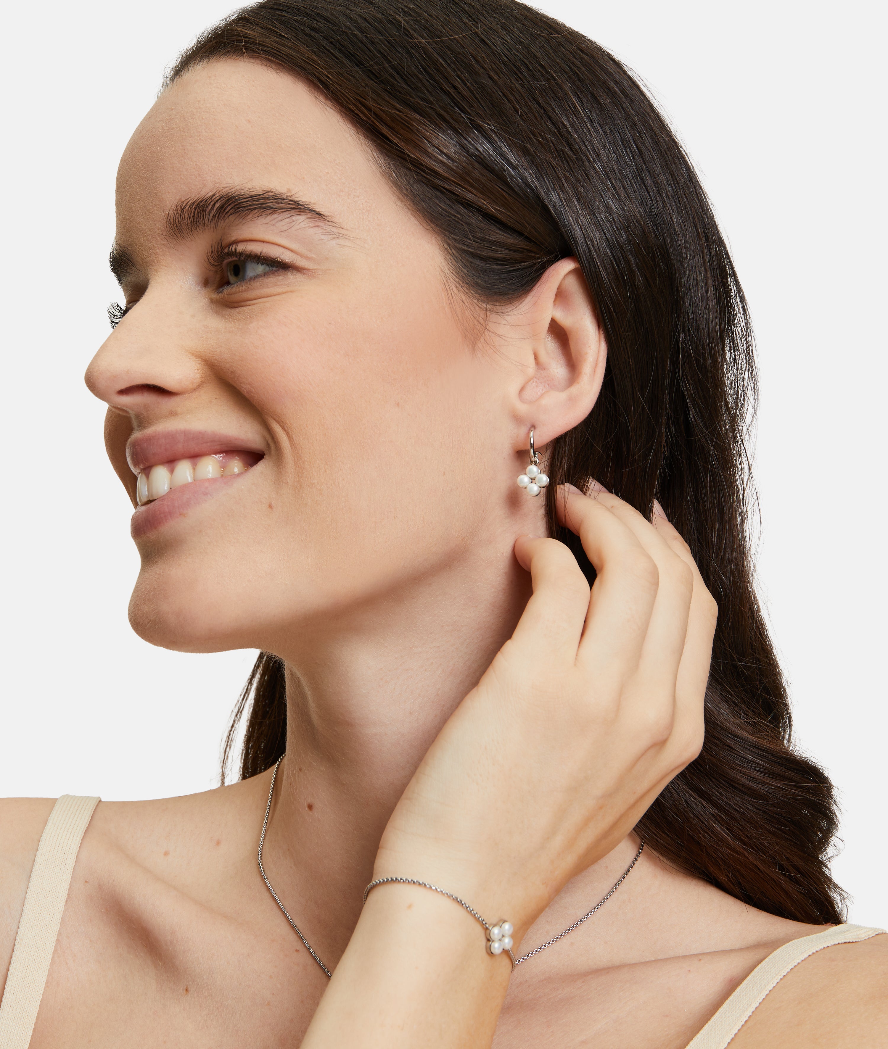 Eine Frau trägt Tamaris Creole - The Flower Pearl Ohrringe mit floralem Design und schimmernden Glasperlen von Tamaris.
