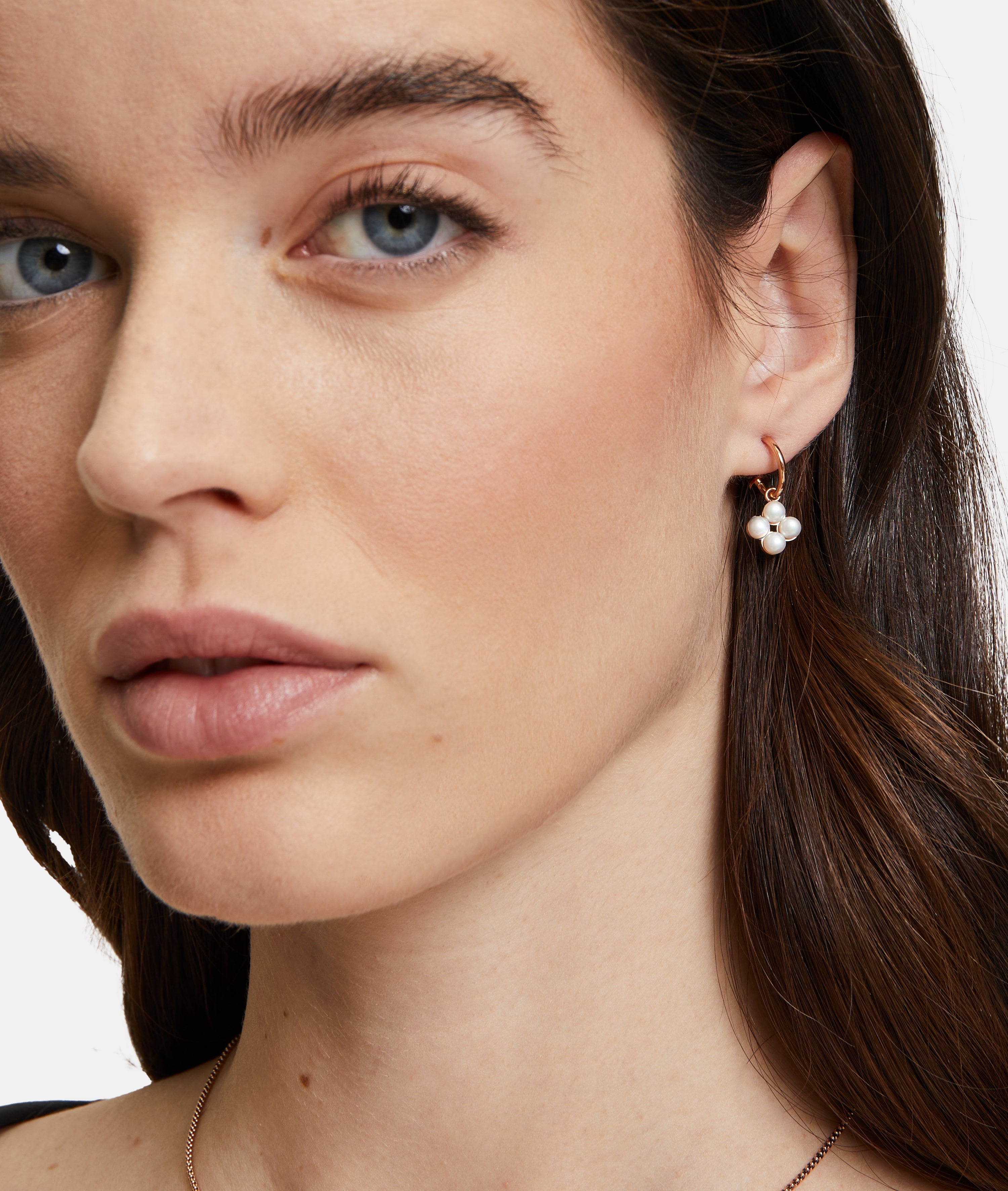 Nahaufnahme einer Frau mit braunen Haaren und natürlichem Make-up, die den Ohrring Tamaris Creole - The Flower Pearl von Tamaris mit floralem Muster trägt, gepaart mit einer dezenten Halskette.