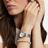 Eine Frau, die eine Tamaris The Small Classic Armbanduhr und ein Perlenarmband trägt, stützt ihre Hand auf ihr Gesicht.