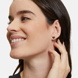 Eine Frau lächelt und berührt ihr Ohr. Sie trägt den Tamaris Ohrstecker - The T-Pattern Heart von Tamaris - perfekt als Geschenk, das von Herzen kommt.