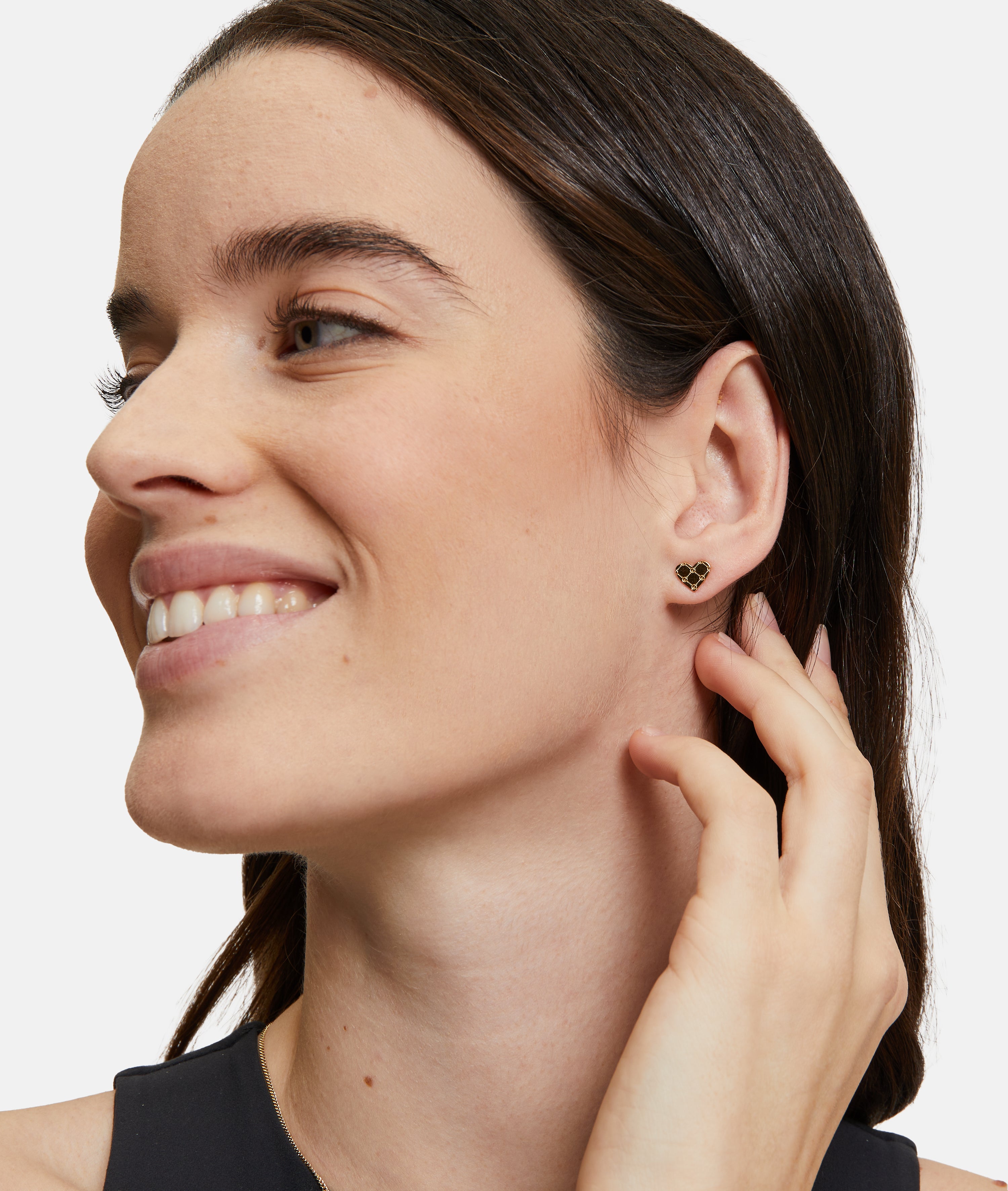 Eine Frau lächelt und berührt ihr Ohr. Sie trägt den Tamaris Ohrstecker - The T-Pattern Heart von Tamaris - perfekt als Geschenk, das von Herzen kommt.