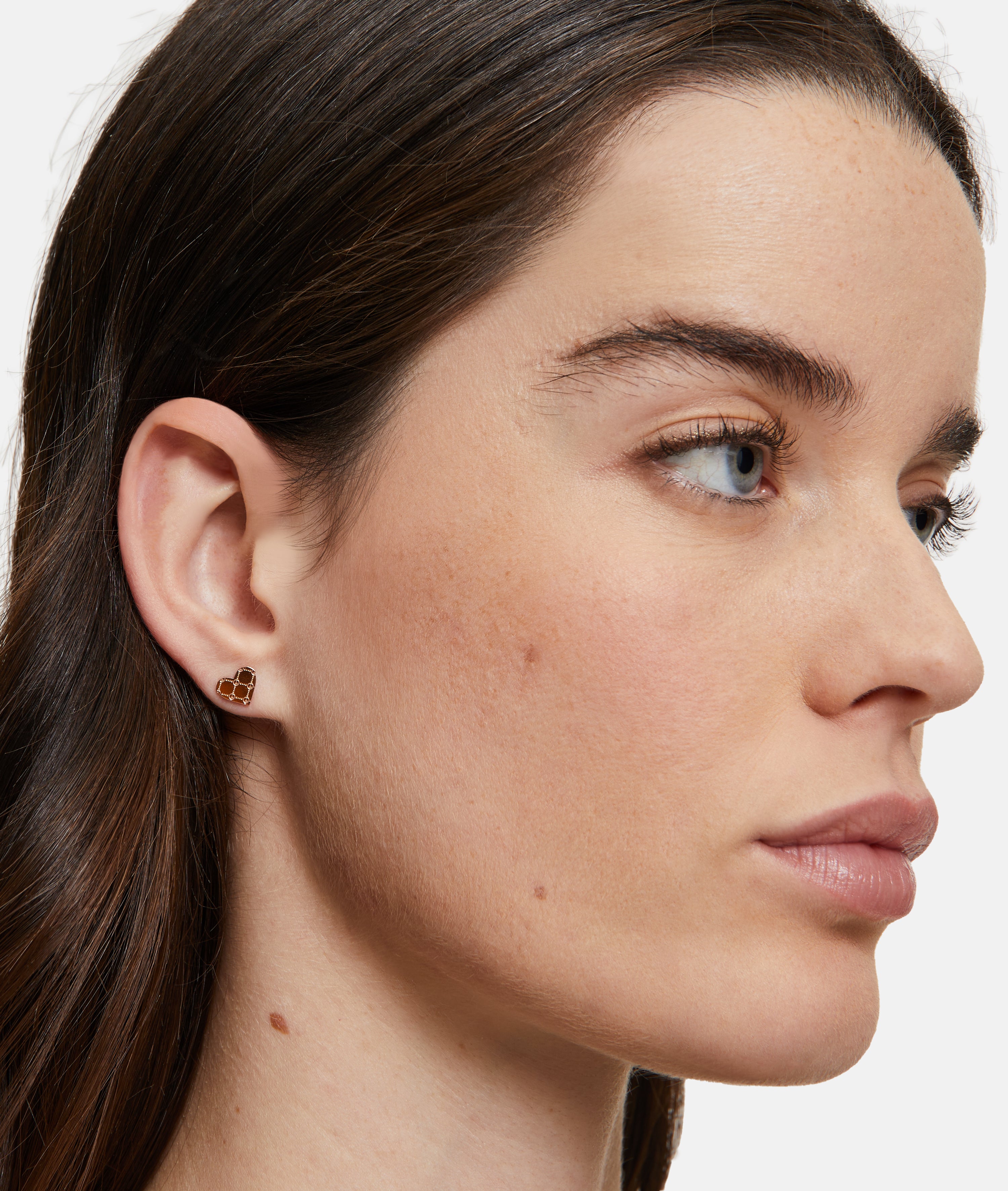 Eine Frau mit heller Haut und braunem Haar trägt Tamaris Ohrstecker - The T-Pattern Heart: kleine, goldene Ohrringe von Tamaris - perfekt als Geschenk.
