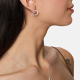 Eine Frau trägt Tamaris Creole - Sparkling Hearts 925 Silber Herz-Ohrringe mit Zirkonia und eine passende Herz-Anhänger-Halskette von Tamaris, ihr Schulter-Tattoo ist sichtbar.