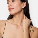 Frau im braunen Oberteil, mit zwei Armtattoos, trägt silberne Ohrringe, eine Tamaris Halskette - Sparkling Hearts von Tamaris mit einem Herzanhänger und ein Armband.