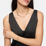 Frau in einem schwarzen, ärmellosen Top, mit einer goldenen Halskette und dem Tamaris Armband - The Edge-einem eleganten Accessoire für Frauen von Tamaris.