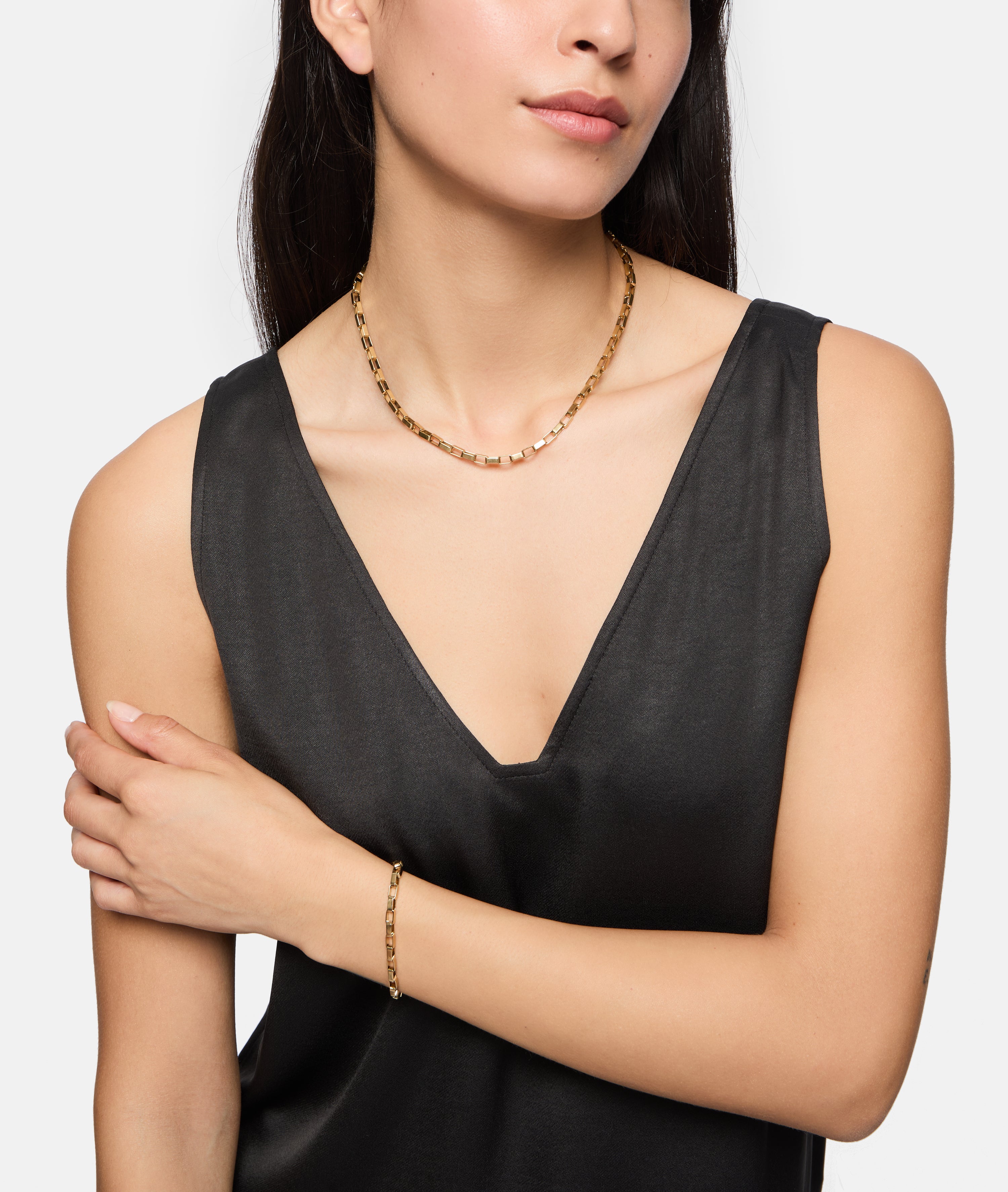 Frau in einem schwarzen, ärmellosen Top, mit einer goldenen Halskette und dem Tamaris Armband - The Edge-einem eleganten Accessoire für Frauen von Tamaris.