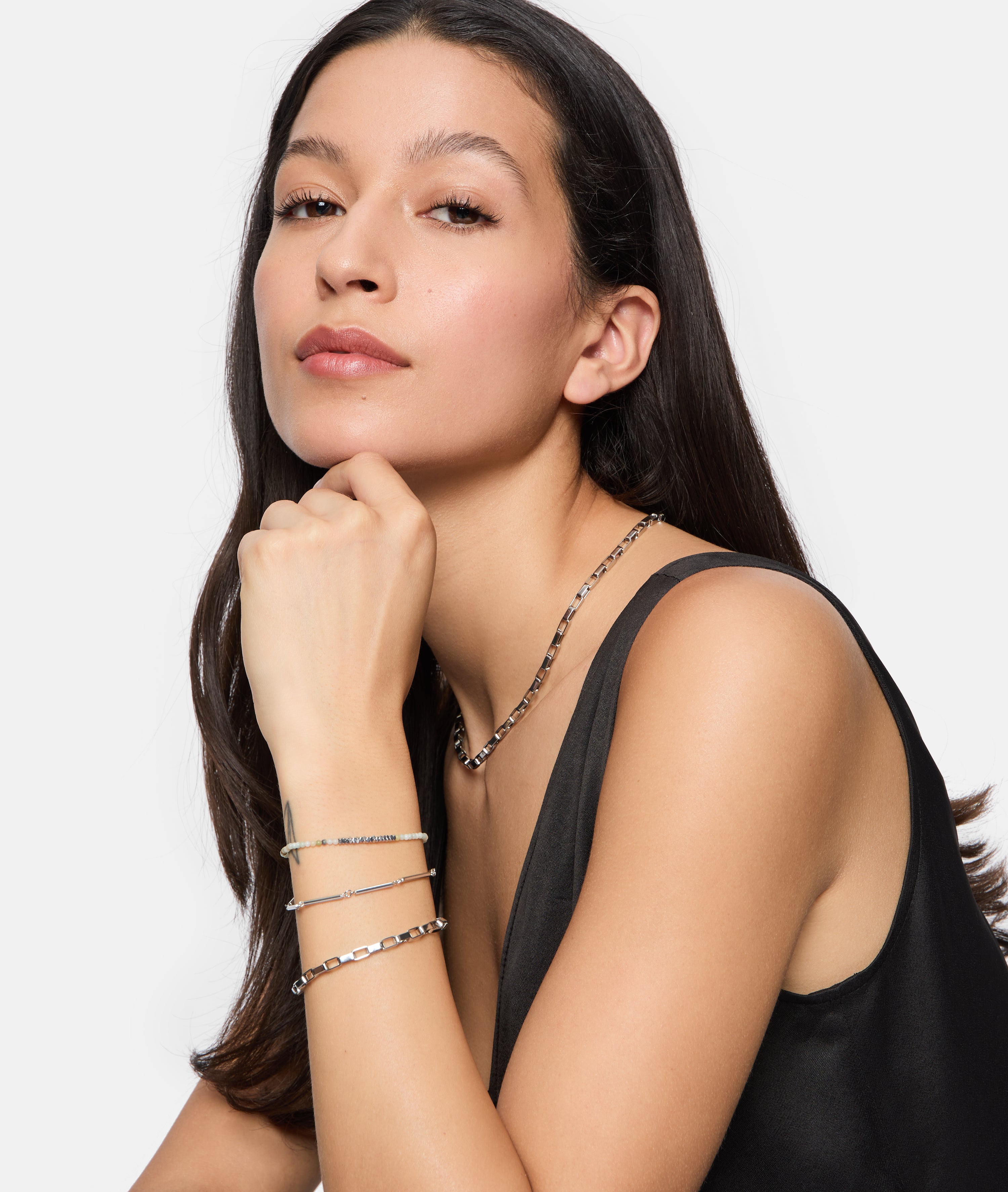 Frau in einem schwarzen Top trägt silbernen Damen Schmuck, darunter das Tamaris Armband - Modern Chain von Tamaris und eine Halskette, während sie nachdenklich posiert.