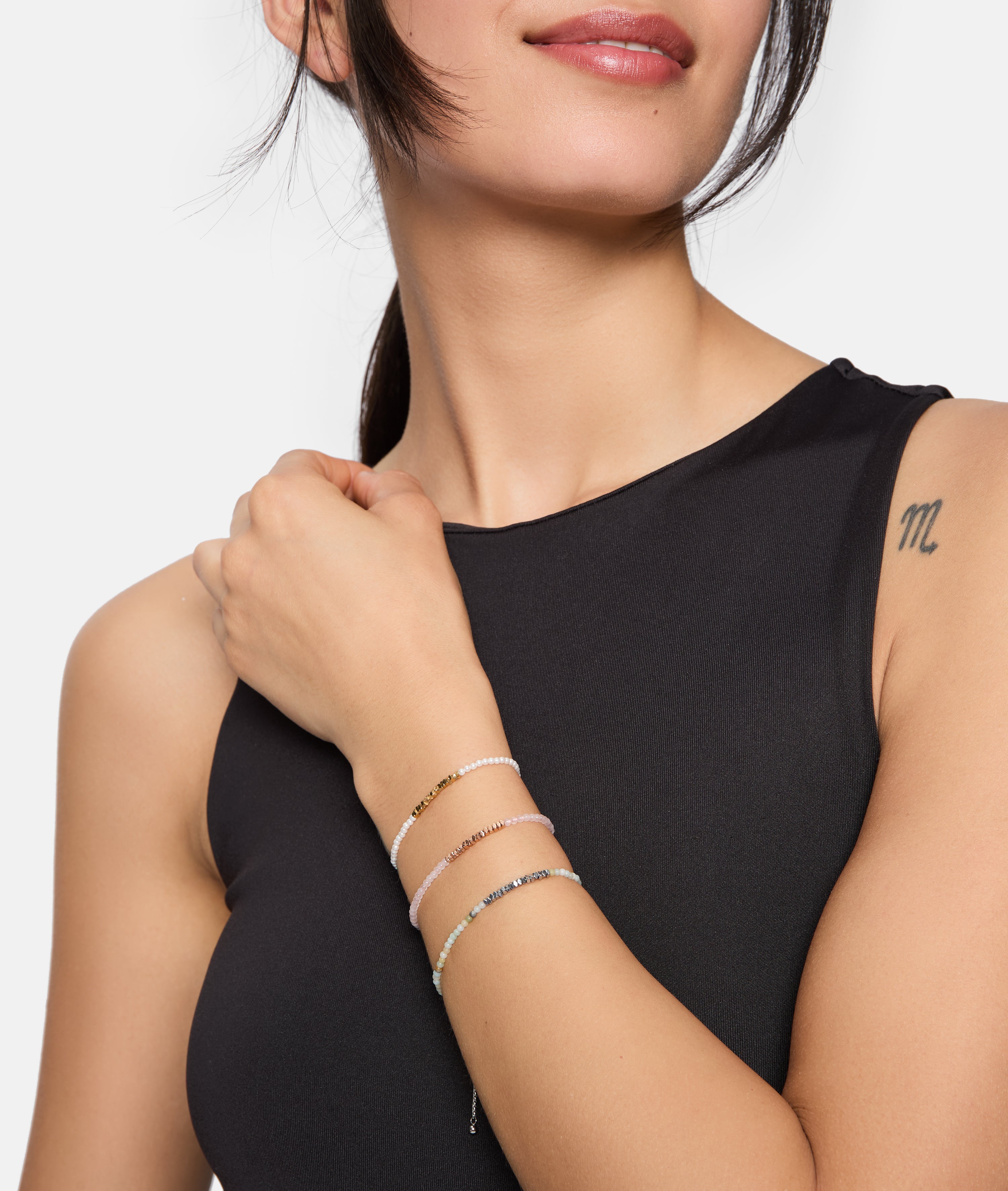 Frau in einem ärmellosen schwarzen Oberteil, die drei Armbänder Tamaris Armband - Modern Pearl Fusion und ein m-Tattoo auf der Schulter trägt.