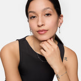 Eine Frau mit langen dunklen Haaren, einem ärmellosen schwarzen Oberteil und dezentem Make-up posiert selbstbewusst und trägt die Tamaris Halskette - Tiny Tubes von Tamaris als elegantes Accessoire.