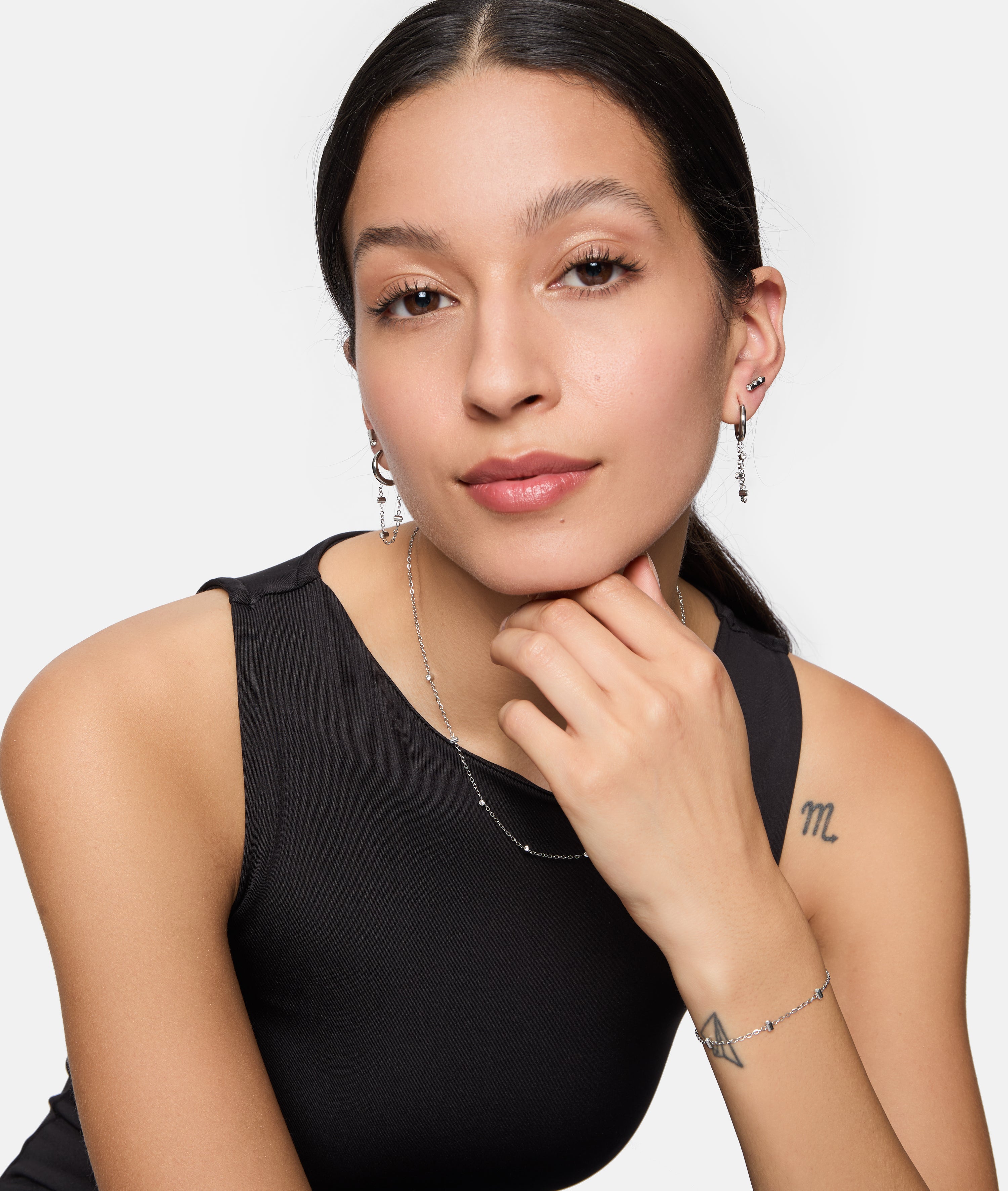 Eine Frau mit langen dunklen Haaren, einem ärmellosen schwarzen Oberteil und dezentem Make-up posiert selbstbewusst und trägt die Tamaris Halskette - Tiny Tubes von Tamaris als elegantes Accessoire.