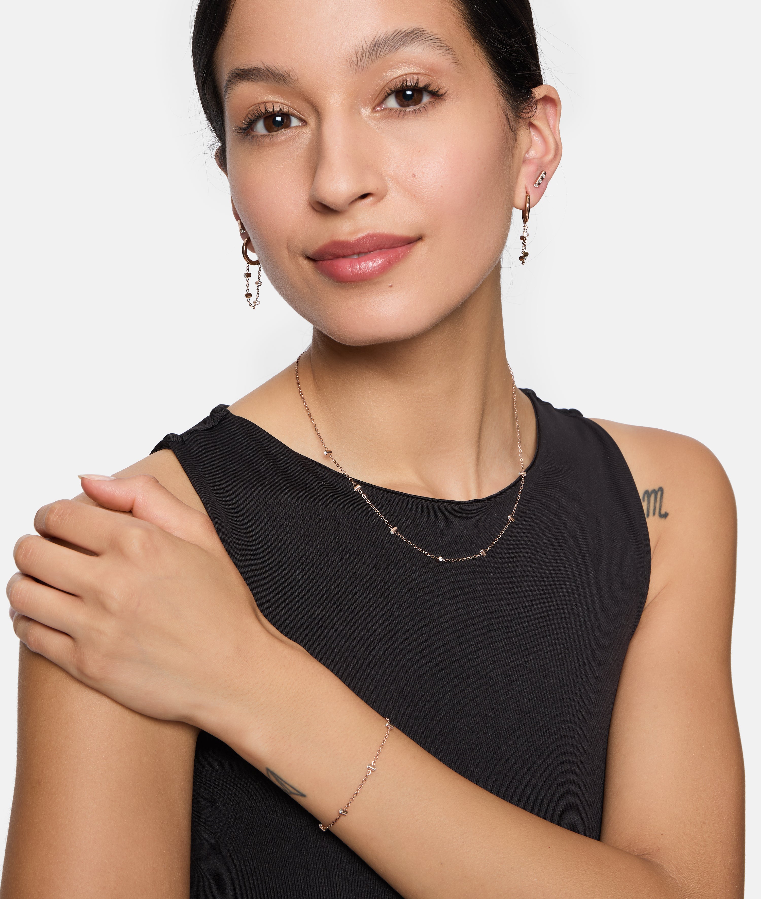 Eine Frau in einem schwarzen ärmellosen Top lächelt in die Kamera. Sie trägt eine passende Tamaris Halskette, ein Armband und Tamaris Tiny Tubes Ohrstecker mit funkelnden Glassteinen.
