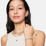 Frau mit langen braunen Haaren trägt eine Tamaris Halskette - Modern Layering, ein Damen Schmuck Armband und ein ärmelloses Top, das ein "m"-Tattoo zeigt.
