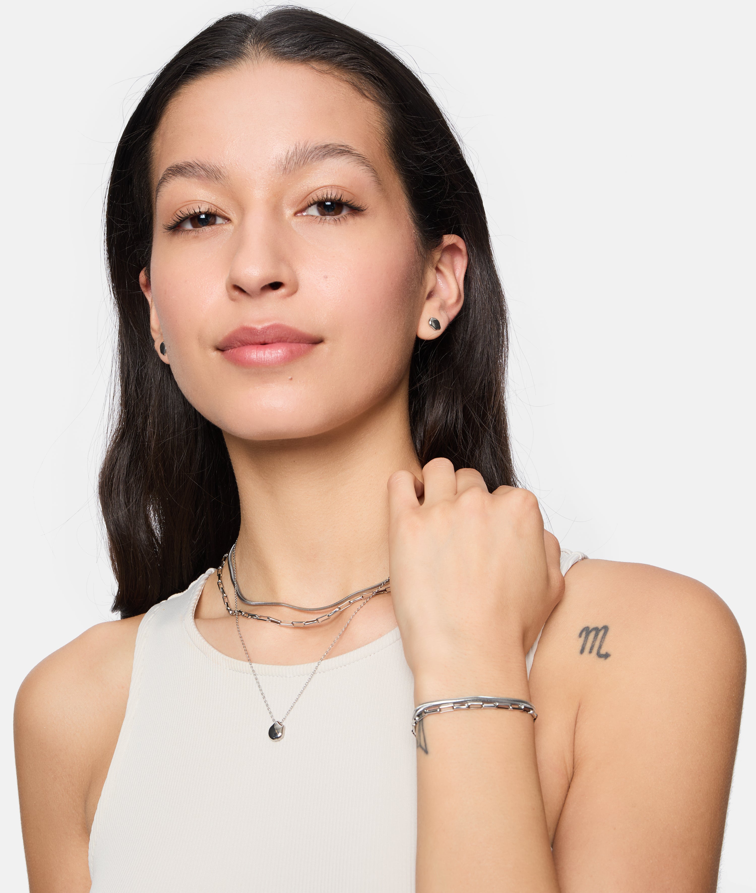Frau mit langen braunen Haaren trägt eine Tamaris Halskette - Modern Layering, ein Damen Schmuck Armband und ein ärmelloses Top, das ein "m"-Tattoo zeigt.
