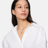 Frau im weißen Hemd trägt Tamaris Ohrstecker - Modern Layering by Tamaris und zwei goldene Halsketten mit organischem Muster, leicht zur Seite schauend.