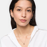Frau mit langen dunklen Haaren und weißem Hemd trägt Tamaris Ohrstecker - Modern Layering by Tamaris und eine Anhänger-Halskette mit organischem Design und schaut in die Kamera.