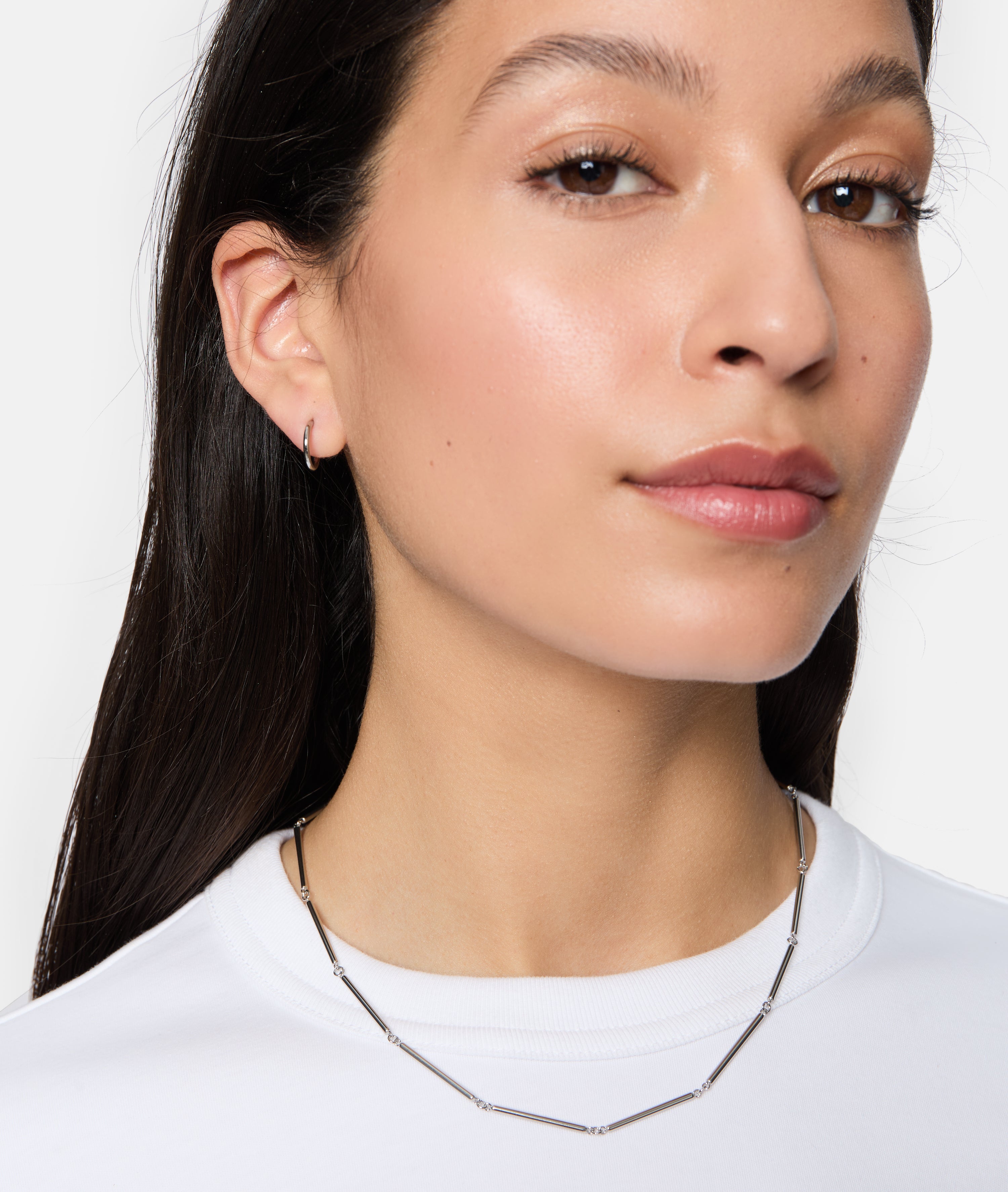 Frau mit der Tamaris Halskette - Modern Chain und kleinen Ohrringen, bekleidet mit einem weißen Top, blickt selbstbewusst nach vorne - das perfekte Schmuckstück von Tamaris für Frauen.