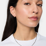 Frau mit dünner Silberkette und Tamaris Creole - Modern Chain Ohrringen von Tamaris, bekleidet mit einem weißen Hemd, vor einem schlichten Hintergrund.