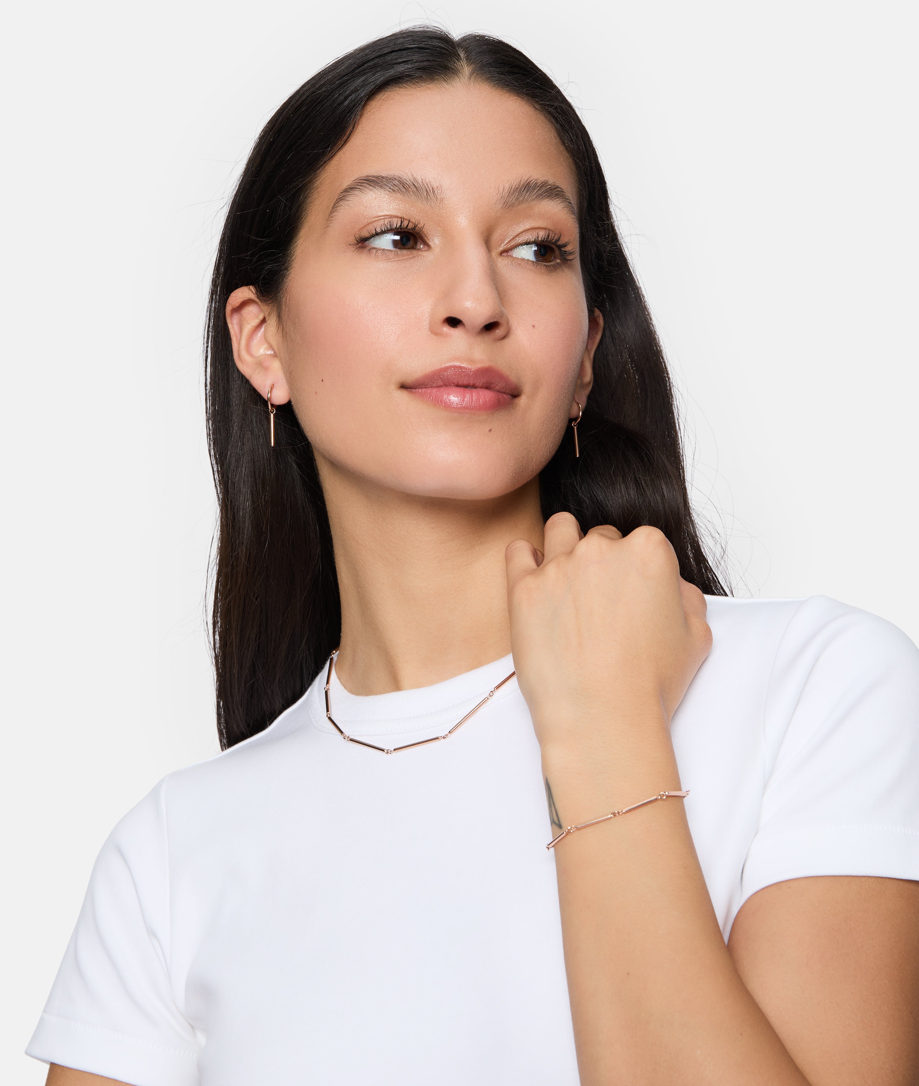 Eine Frau in einem weißen Hemd trägt passenden Goldschmuck von Tamaris, darunter die Tamaris Halskette - Modern Chain, zusammen mit einem Armband und Ohrringen, mit Blick zur Seite.