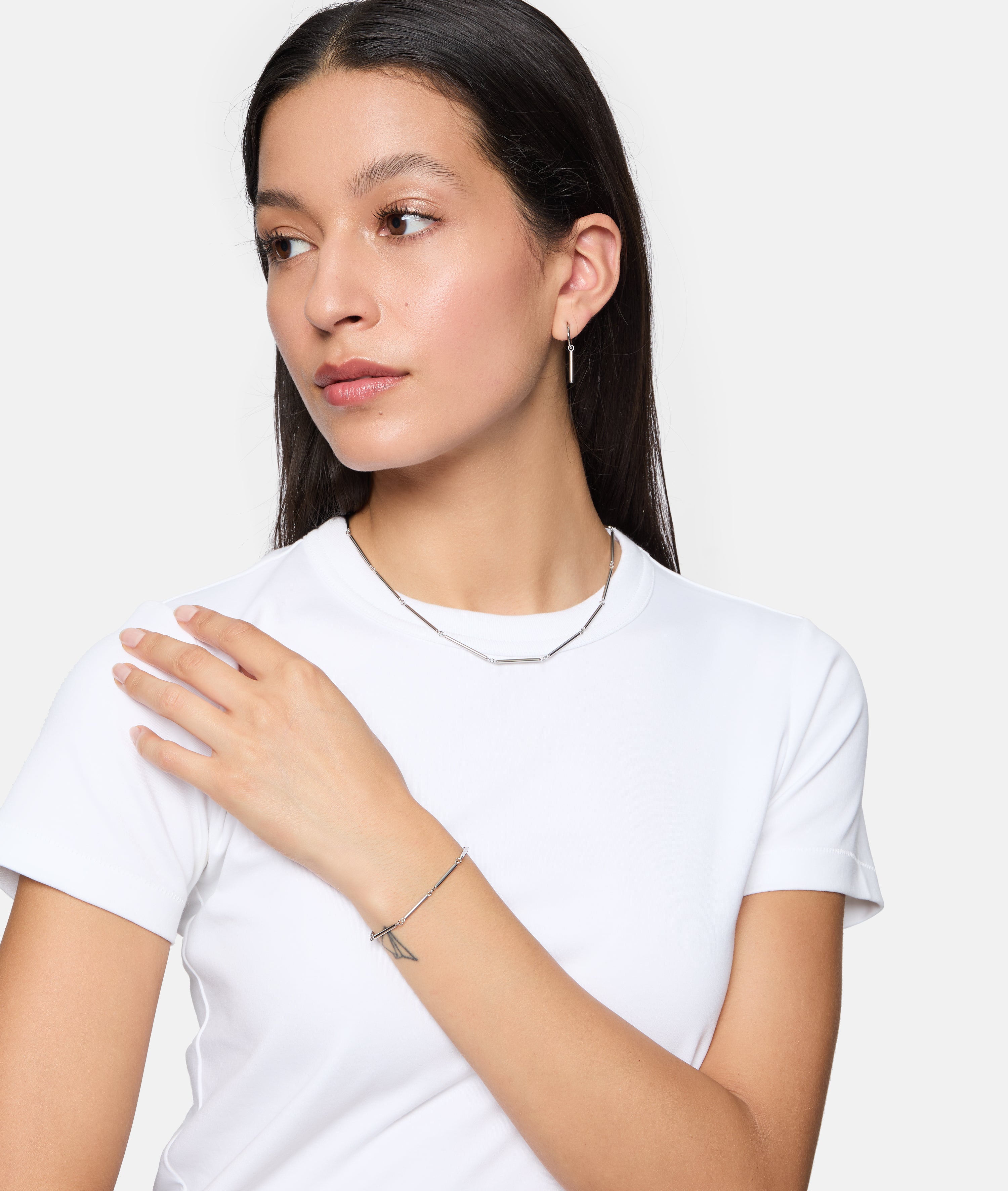 Frau in weißem T-Shirt trägt Tamaris Damen Schmuck, darunter das Tamaris Armband - Modern Chain, schaut mit der Hand auf der Schulter zur Seite.