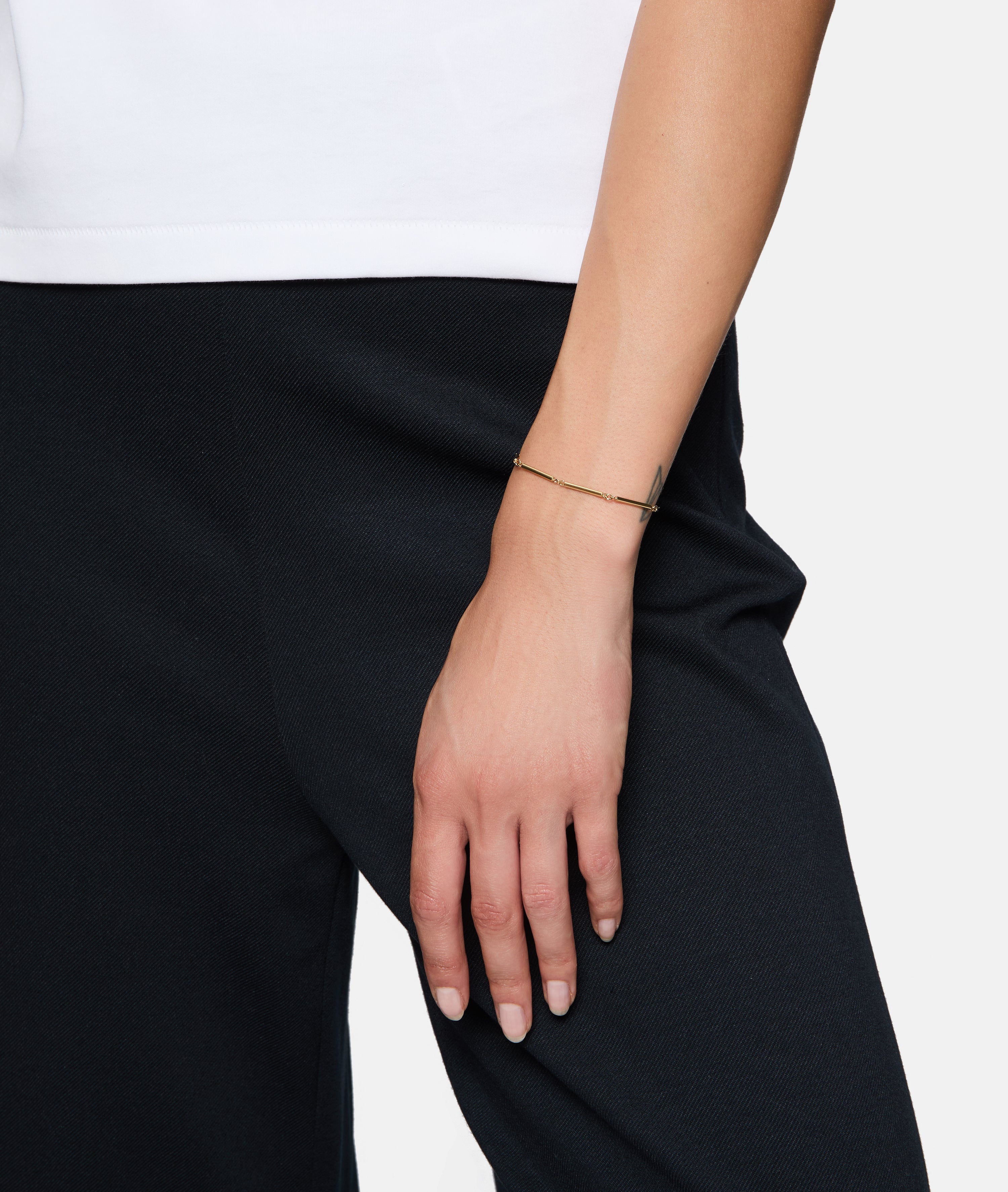 Eine Person, die eine schwarze Hose und ein weißes Oberteil trägt, mit dem Tamaris Armband - Modern Chain, einem stilvollen Armband von Tamaris, an ihrem Handgelenk.