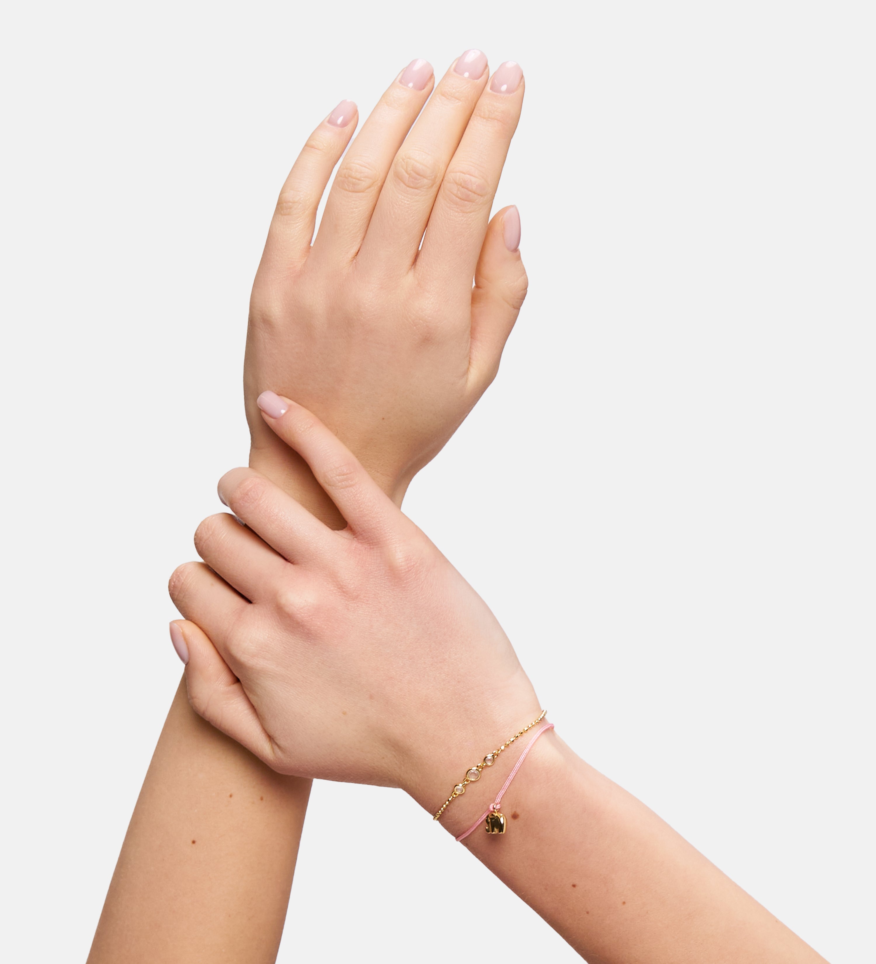 Zwei überkreuzte Hände mit zartem rosafarbenem Armband und goldenem Anhänger in Herzform