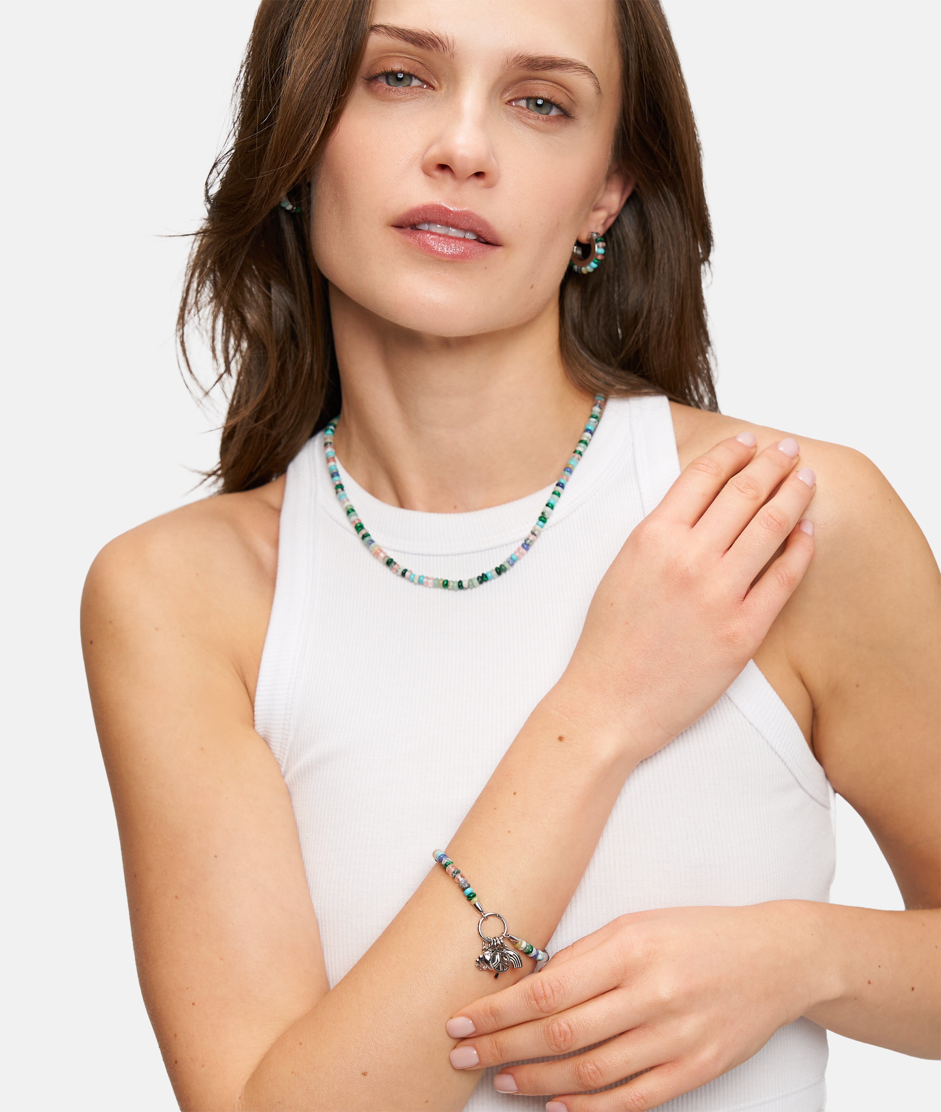 Frau in einem weißen, ärmellosen Oberteil, mit passender Perlenkette und Ohrringen, ausgestattet mit dem Tamaris Armband - All About Beads by Tamaris, und mit einem sanften Lächeln posierend.