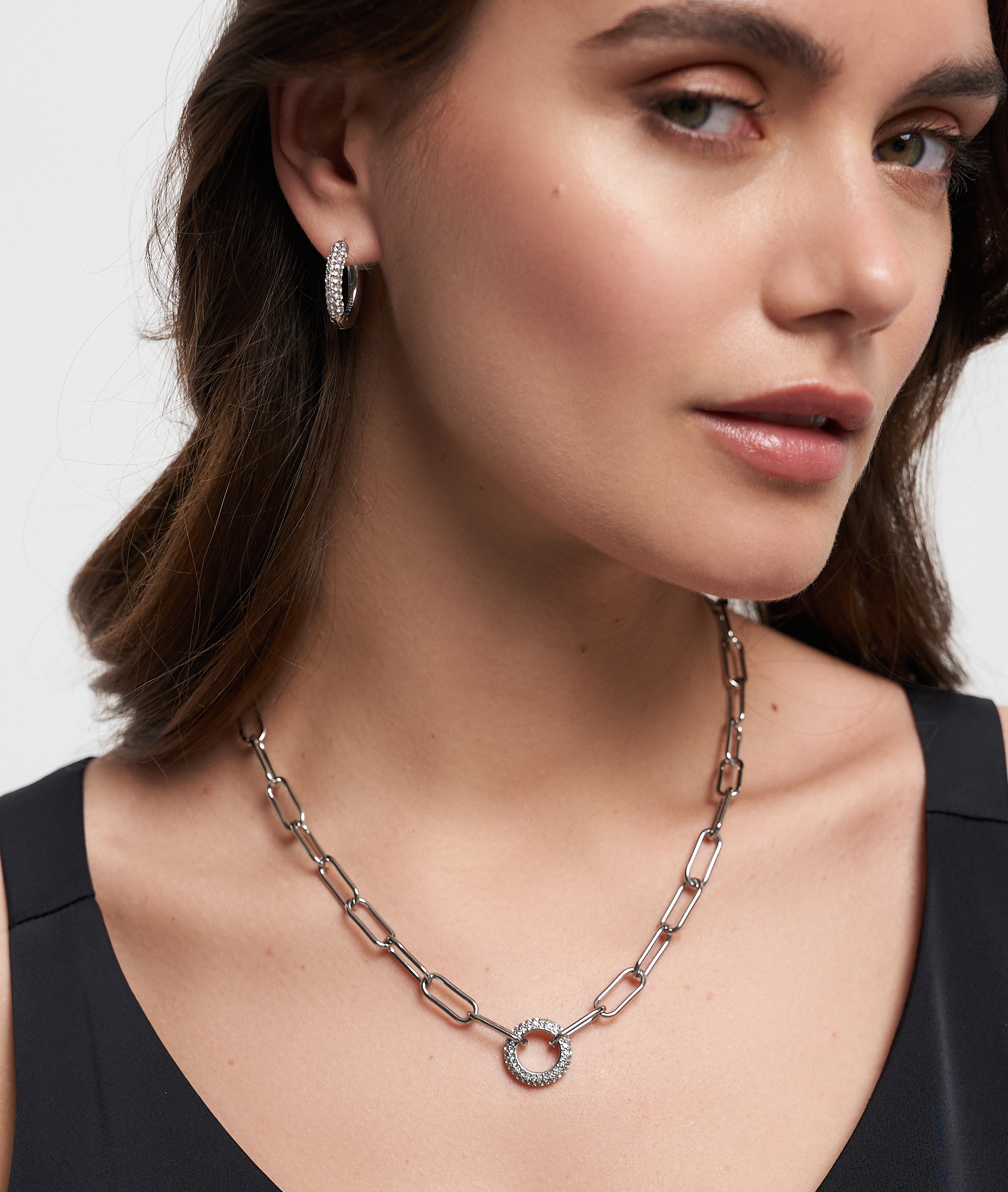 Eine elegant in Schwarz gekleidete Frau trägt die Tamaris Halskette - Glitter Donuts und dazu passende Creolen, alles von Tamaris in modernem Design.