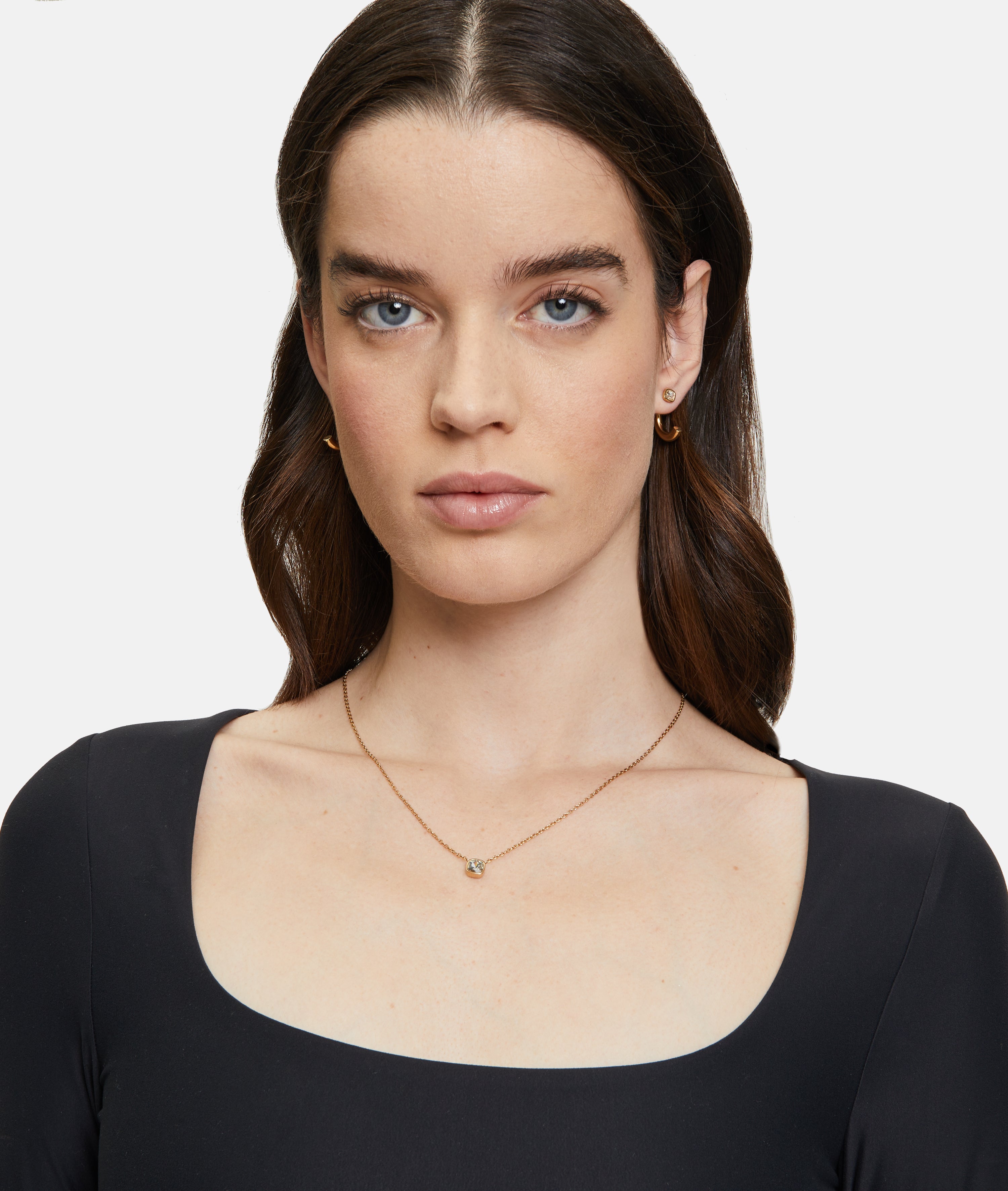 Frau mit langen braunen Haaren trägt ein schwarzes Oberteil mit quadratischem Ausschnitt, goldene Ohrringe und das Tamaris Set - The Layer Collier von Tamaris.