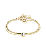 Das Tamaris Set - The Layer von Tamaris besteht aus einem goldenen Kettenarmband mit einem klaren Edelstein in der Mitte und einem verstellbaren Verschluss, der von der Eleganz der Schlangenkette inspiriert ist und auf einem weißen Hintergrund steht.