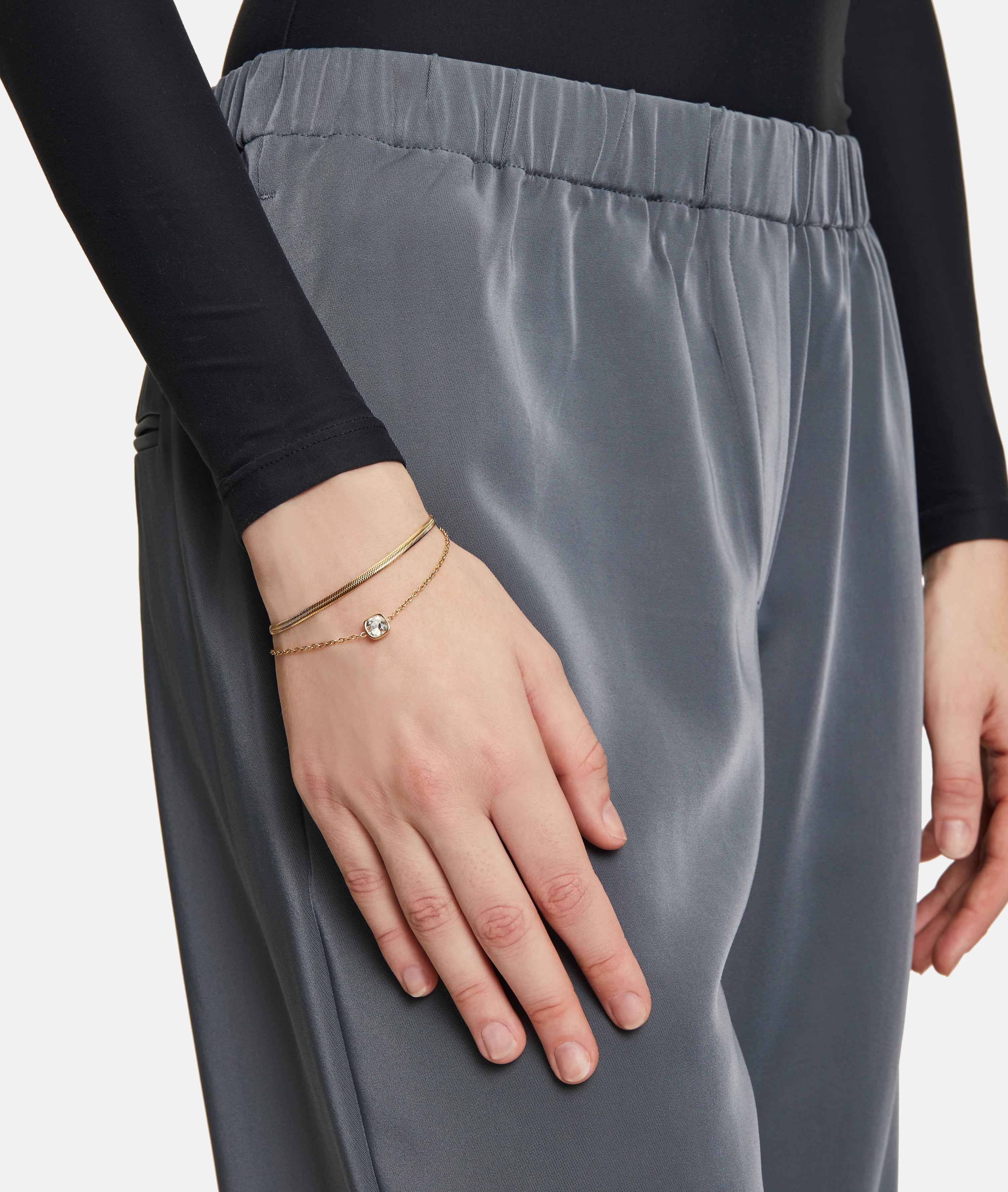 Eine Person, die eine graue Satinhose und ein Tamaris Set - The Layer von Tamaris trägt, stützt ihre Hand auf ihr Bein.
