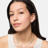 Eine Frau mit langen dunklen Haaren trägt Ohrstecker, eine Tamaris Halskette - Modern Layering und ein weißes Tanktop, während sie in die Kamera schaut.