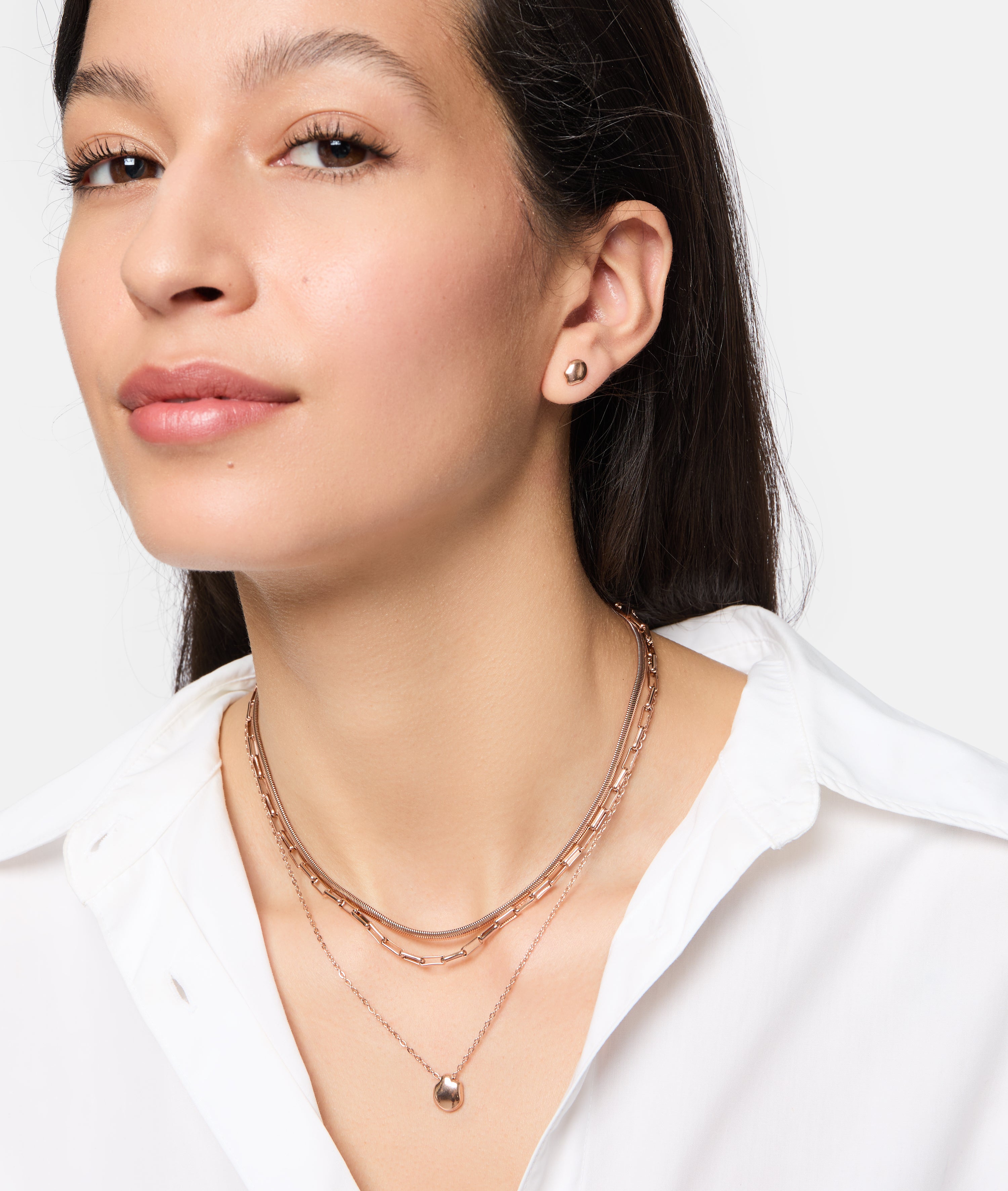 Frau mit langen braunen Haaren trägt die Tamaris Halskette - Modern Layering von Tamaris und ein weißes Button-up-Hemd und posiert selbstbewusst.