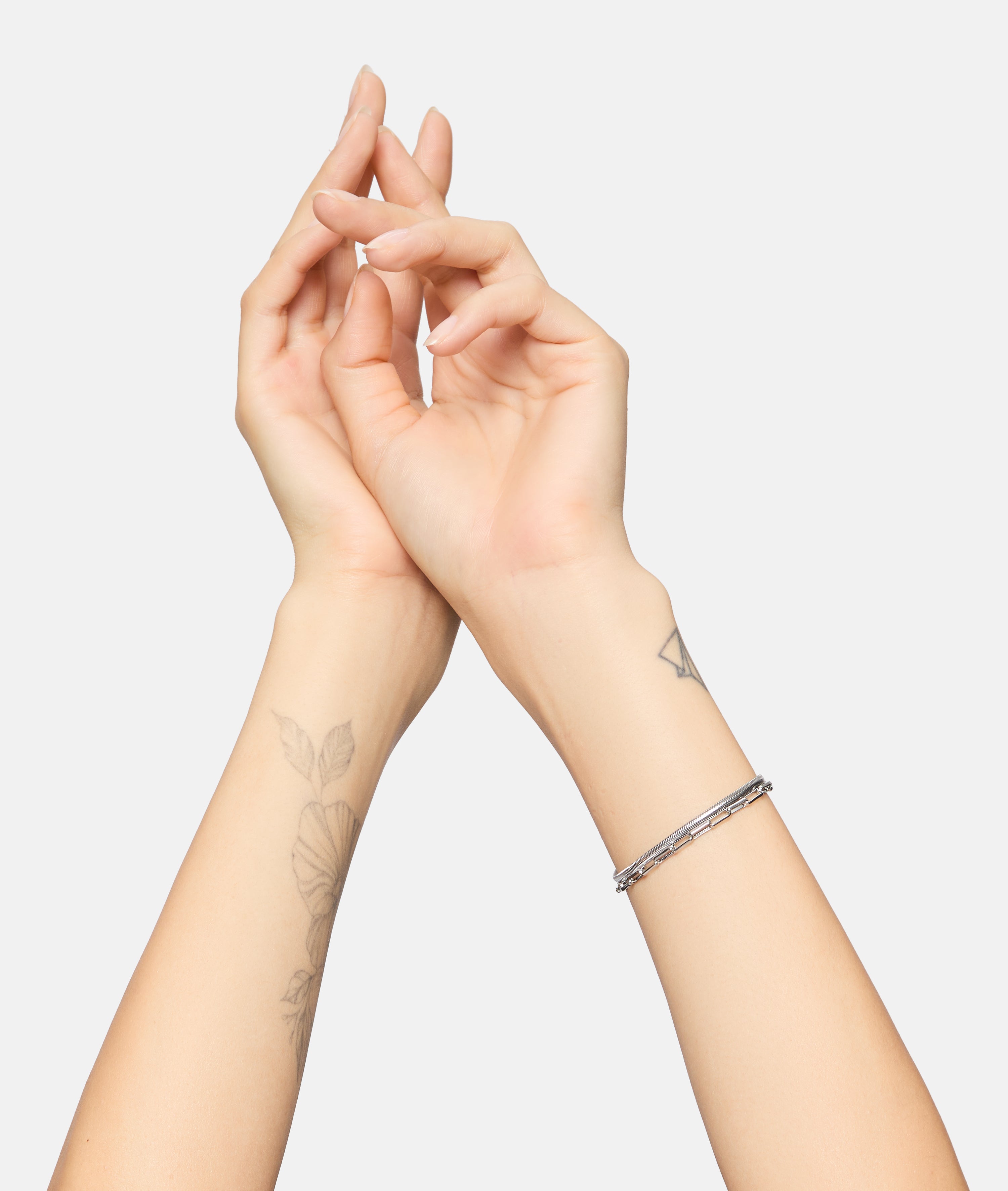 Zwei Hände mit floralen Tattoos tragen ein Tamaris Armband - Modern Layering Armband von Tamaris an einem Handgelenk, posiert vor einem schlichten weißen Hintergrund.