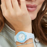 Eine Frau lächelt und trägt die Tamaris Armbanduhr - The Blue Silicone von Tamaris mit einem hellblauen Armband und einem Perlenarmband am Handgelenk.