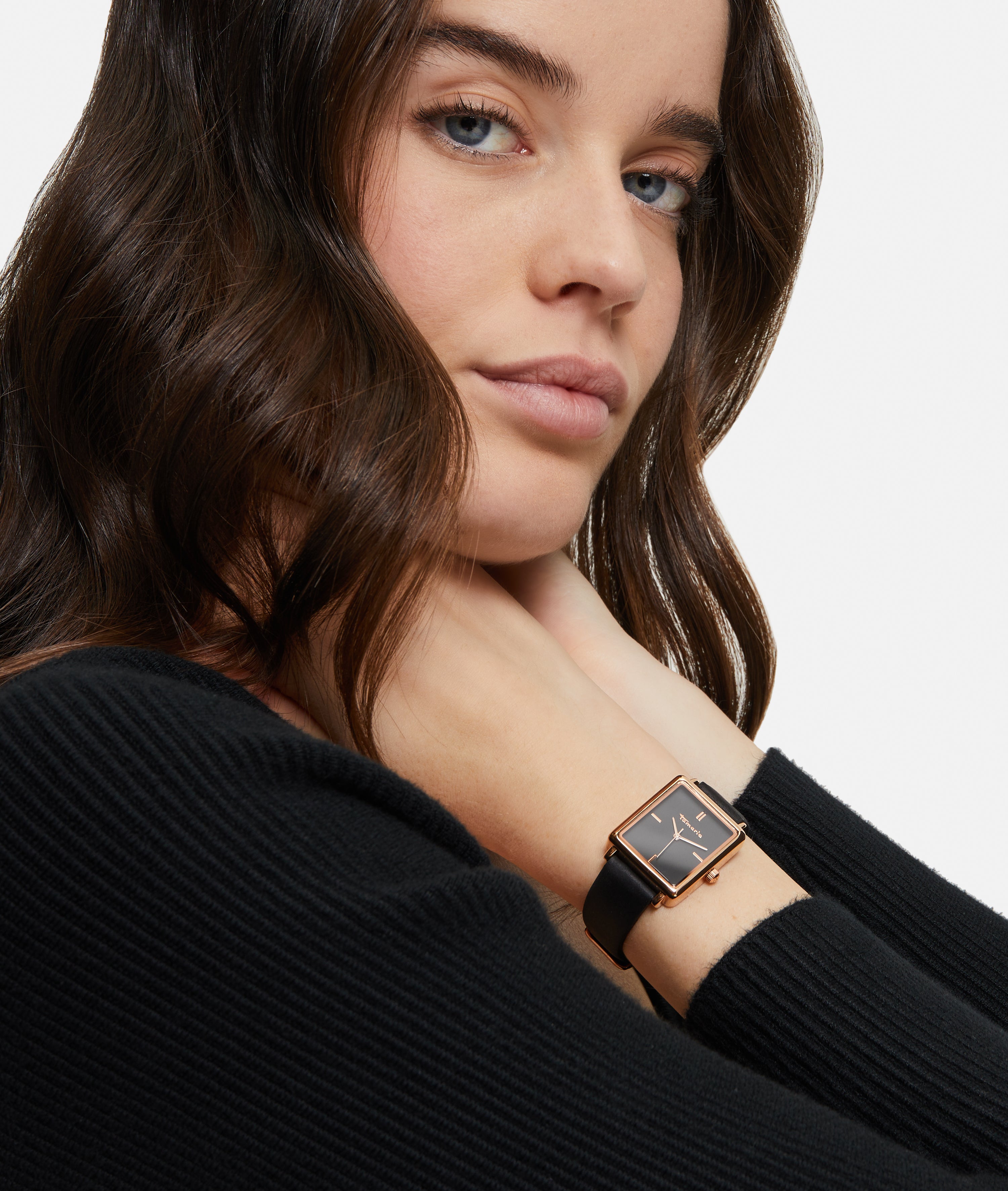 Frau mit langen braunen Haaren in einem schwarzen Pullover trägt die Tamaris Armbanduhr - The Square Black und schaut in die Kamera.