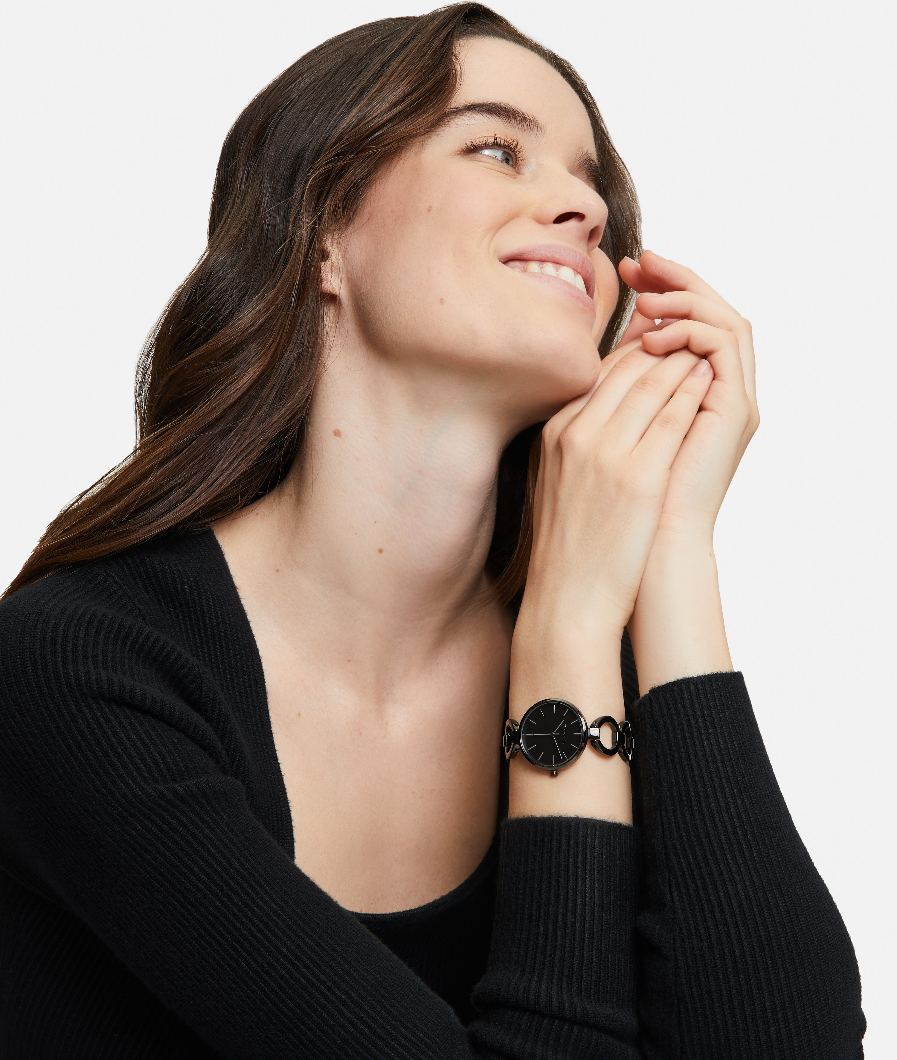 Frau in schwarzem Top, lächelnd, trägt die Tamaris Armbanduhr - The Black Glamorous mit Edelstahlband, die Hände vor dem Gesicht verschränkt.