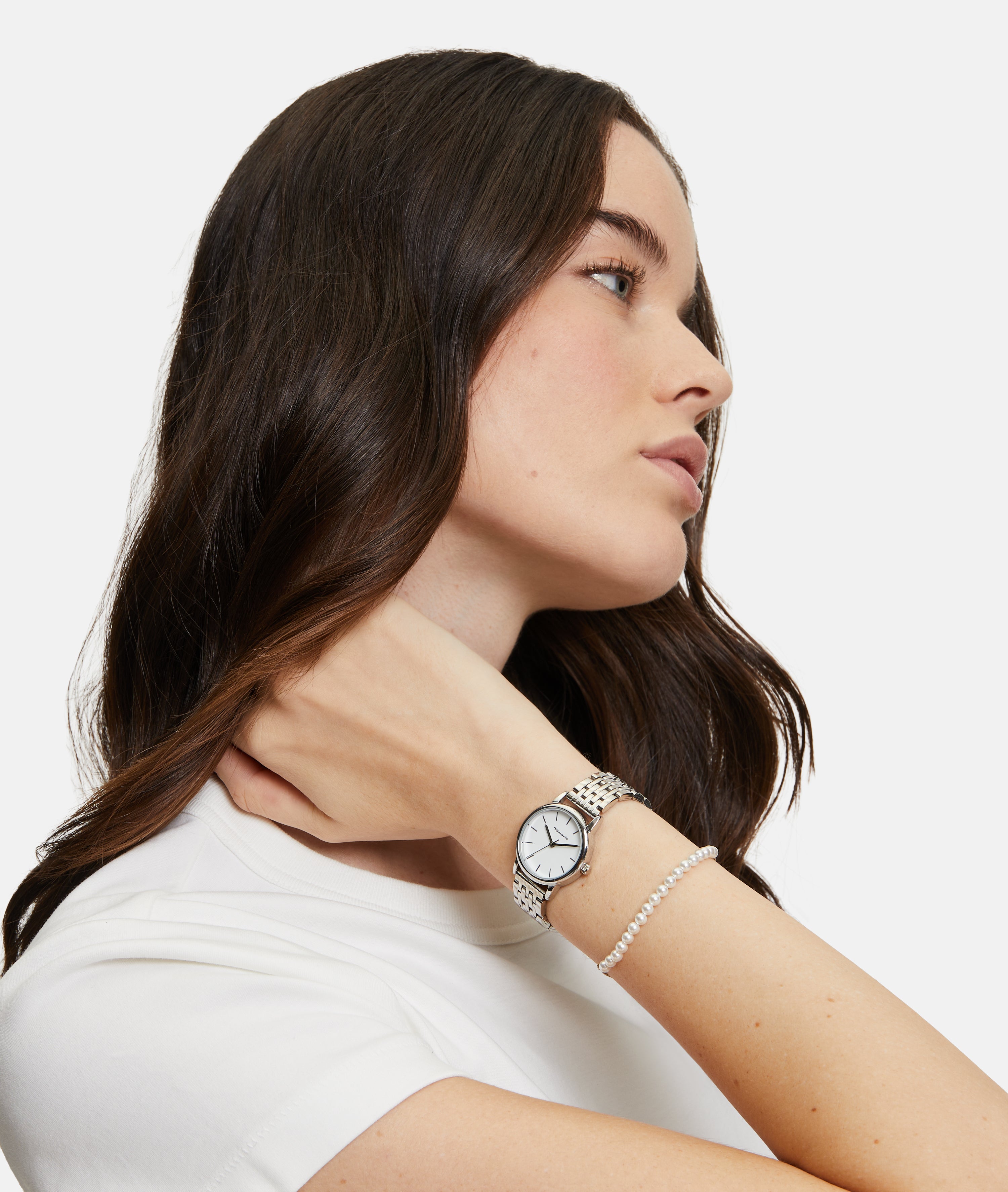 Frau in weißem Hemd trägt die Tamaris Armbanduhr - The Small Classic und ein Perlenarmband, wobei sie ihre Hand elegant in den Nacken legt.