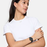 Eine Frau in einem weißen T-Shirt trägt die Tamaris Armbanduhr - Sparkle Up mit elegantem Design und schlankem Meshband am Handgelenk und schaut mit verschränkten Armen zur Seite.