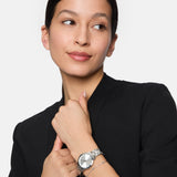 Frau in schwarzem Outfit mit Blick zur Seite, trägt die Tamaris Armbanduhr - The Elegance und ein Armband am linken Handgelenk - ein zeitloses Tamaris-Accessoire, das ihren eleganten Look vervollständigt.