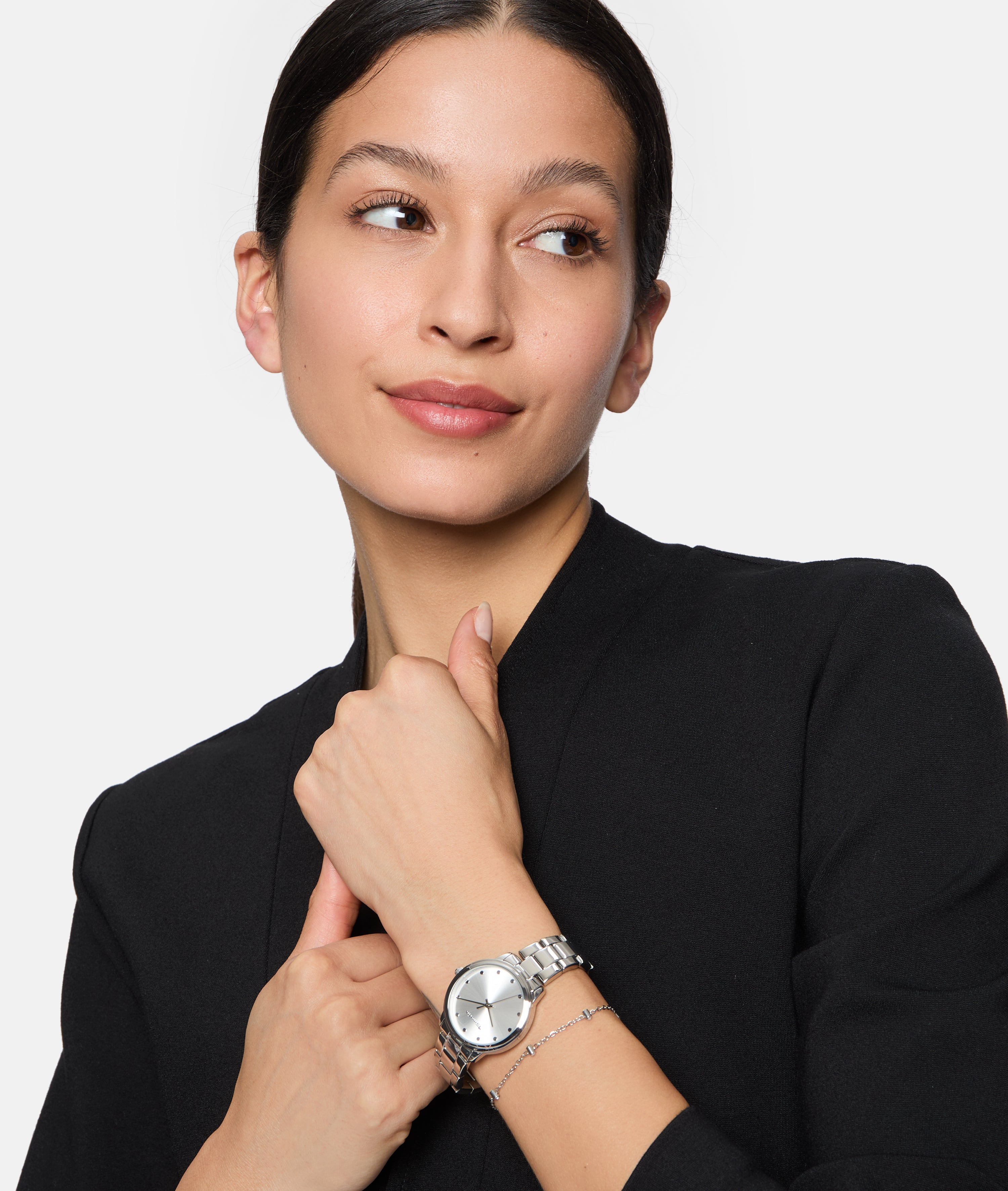 Frau in schwarzem Outfit mit Blick zur Seite, trägt die Tamaris Armbanduhr - The Elegance und ein Armband am linken Handgelenk - ein zeitloses Tamaris-Accessoire, das ihren eleganten Look vervollständigt.
