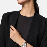 Eine Frau in einem schwarzen Blazer trägt eine silberne Armbanduhr und das Tamaris Armband - Tiny Tubes. Dieses zarte Accessoire von Tamaris ist die perfekte Wahl für Frauen, die ihr Revers berühren.