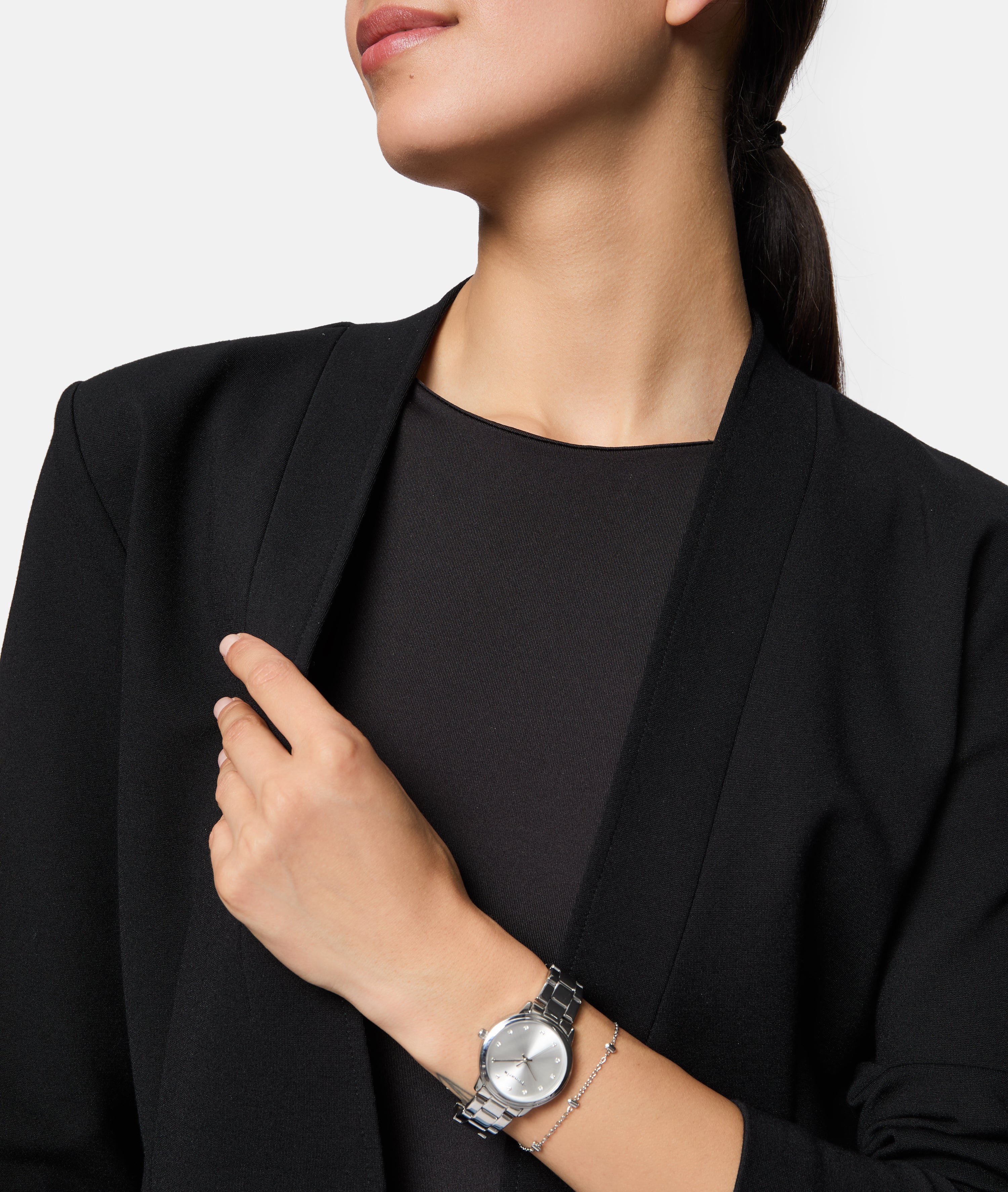 Eine Frau in einem schwarzen Blazer trägt eine silberne Armbanduhr und das Tamaris Armband - Tiny Tubes. Dieses zarte Accessoire von Tamaris ist die perfekte Wahl für Frauen, die ihr Revers berühren.