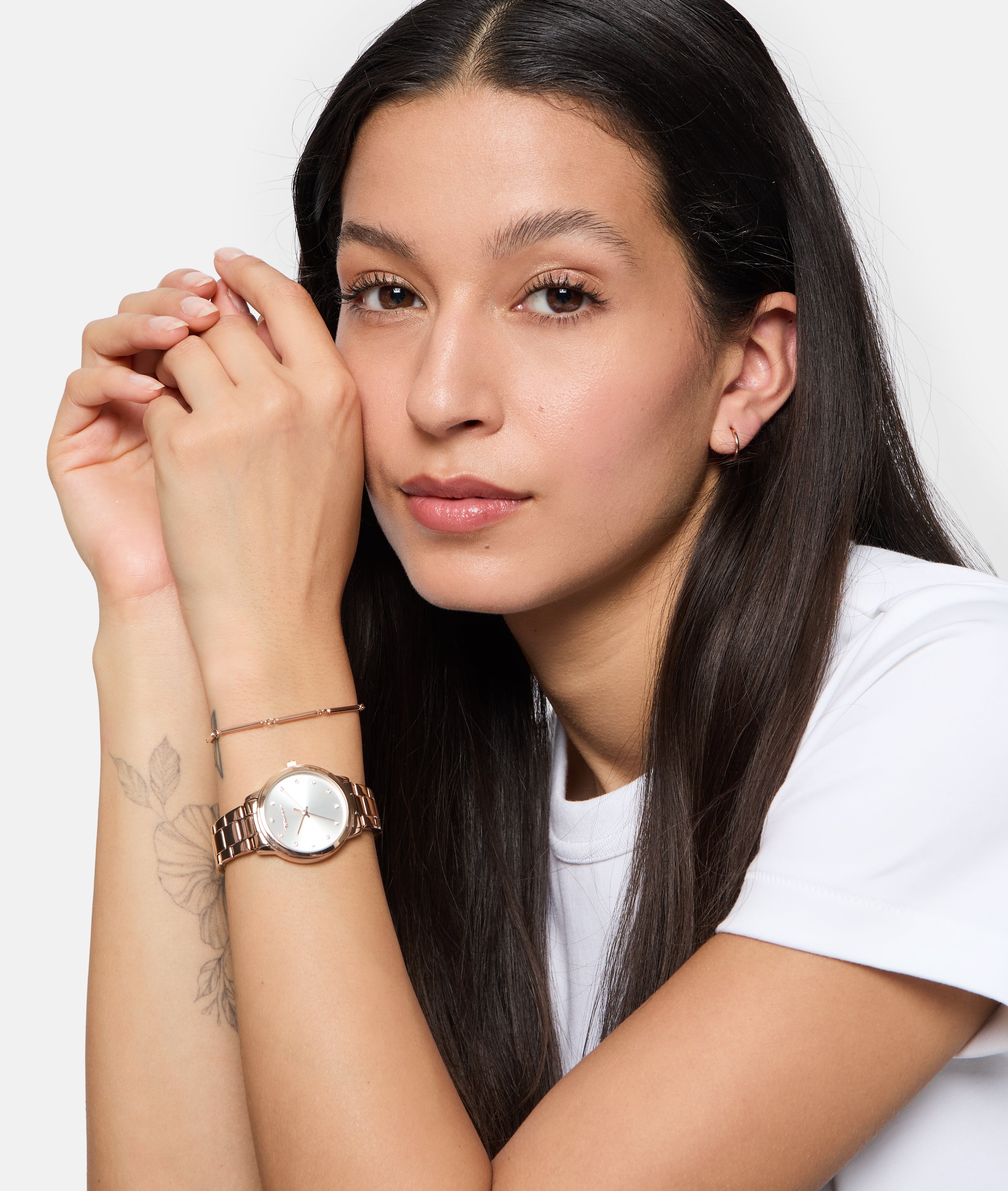 Eine Frau mit langen dunklen Haaren und weißem Hemd zeigt ihre Tamaris Armbanduhr - The Elegance mit funkelnden Zirkoniasteinen und einem eleganten Edelstahlband, während sie ihr Kinn sanft auf ihre Hände stützt.