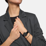 Eine Frau in einem dunklen Blazer trägt die Tamaris Armbanduhr - The Elegance by Tamaris, die Hände vor der Brust gekreuzt - und betont damit dieses zeitlose Accessoire, das ihrem Stil subtile Eleganz verleiht.