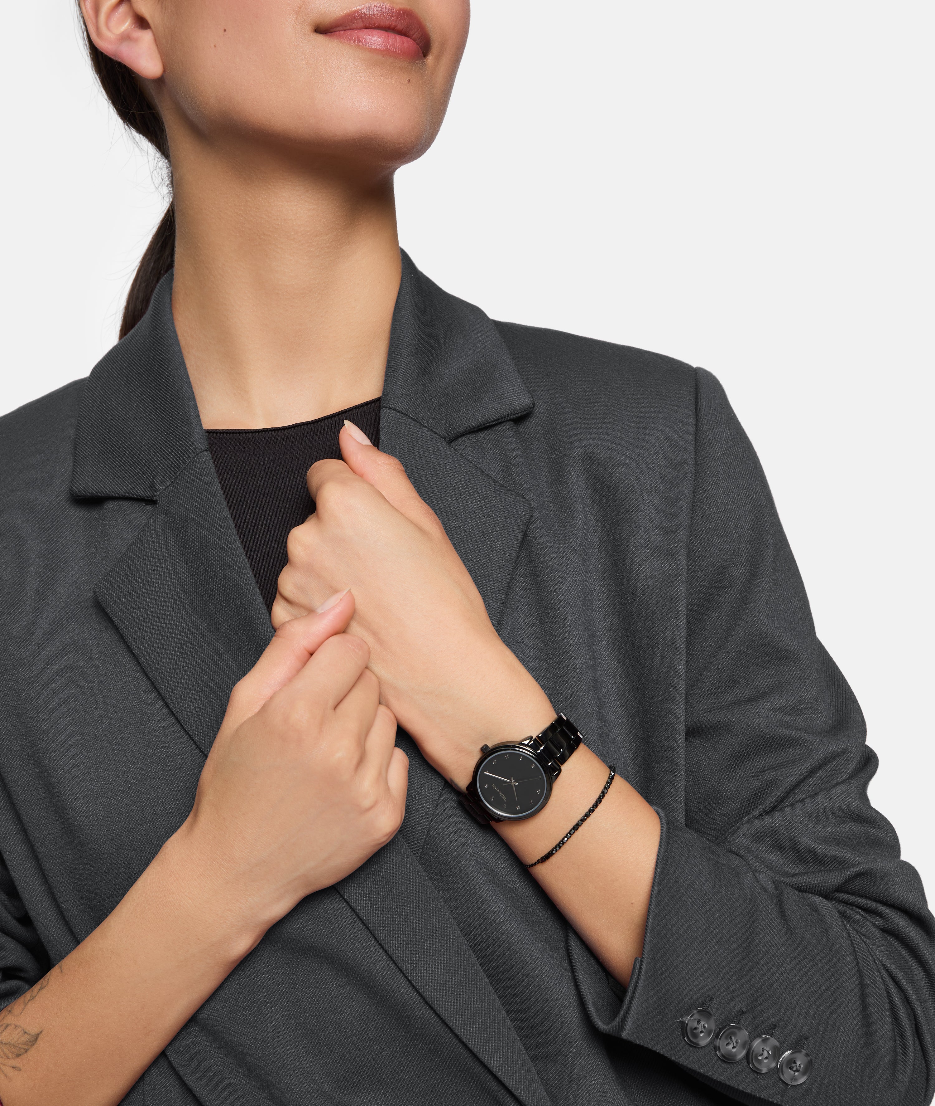 Eine Frau in einem dunklen Blazer trägt die Tamaris Armbanduhr - The Elegance by Tamaris, die Hände vor der Brust gekreuzt - und betont damit dieses zeitlose Accessoire, das ihrem Stil subtile Eleganz verleiht.