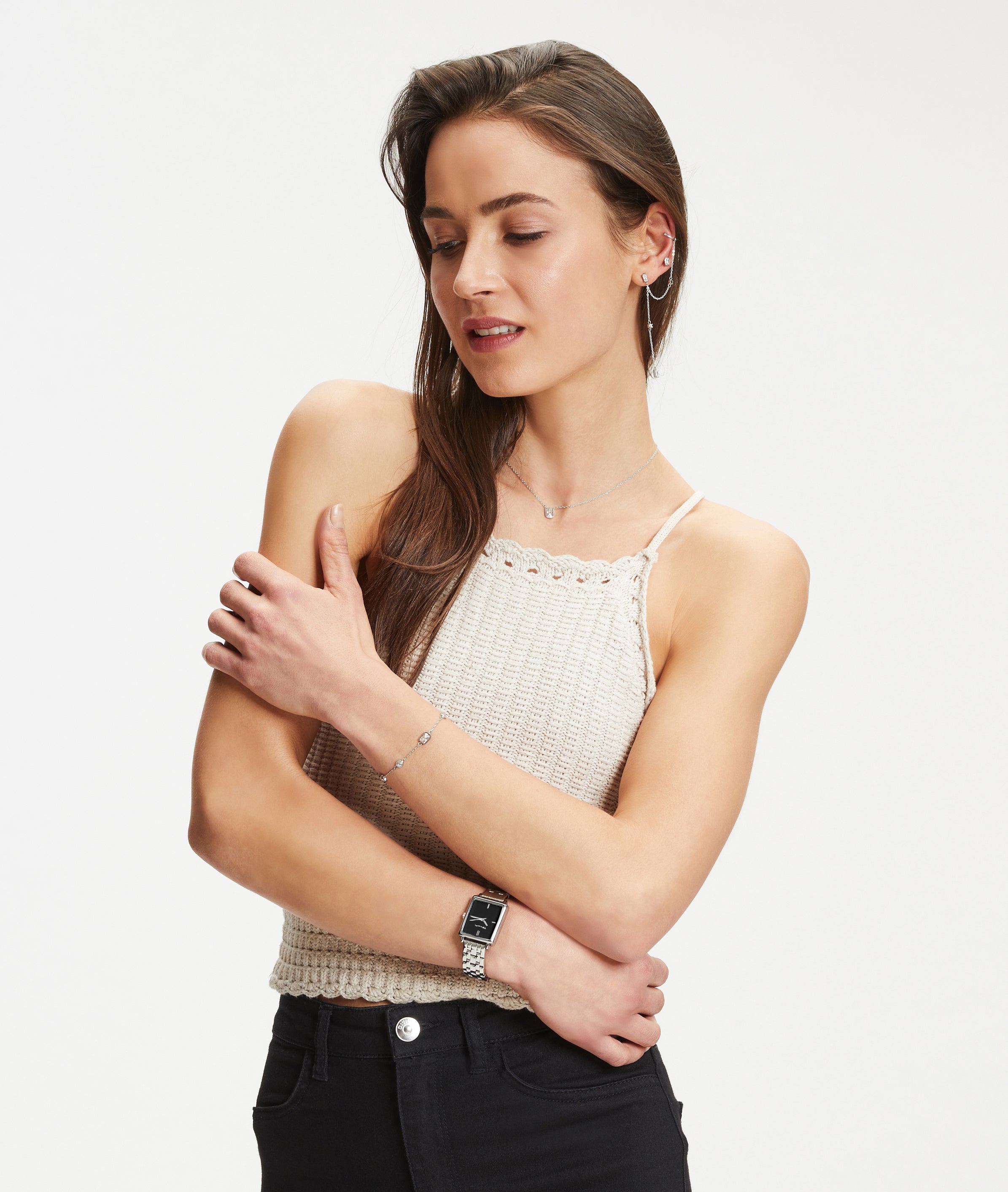 Eine Frau in einem cremefarbenen Strickoberteil und einer schwarzen Hose posiert vor einem weißen Hintergrund und trägt die Tamaris Armbanduhr - The Square von Tamaris für einen klassisch-modernen Stil.